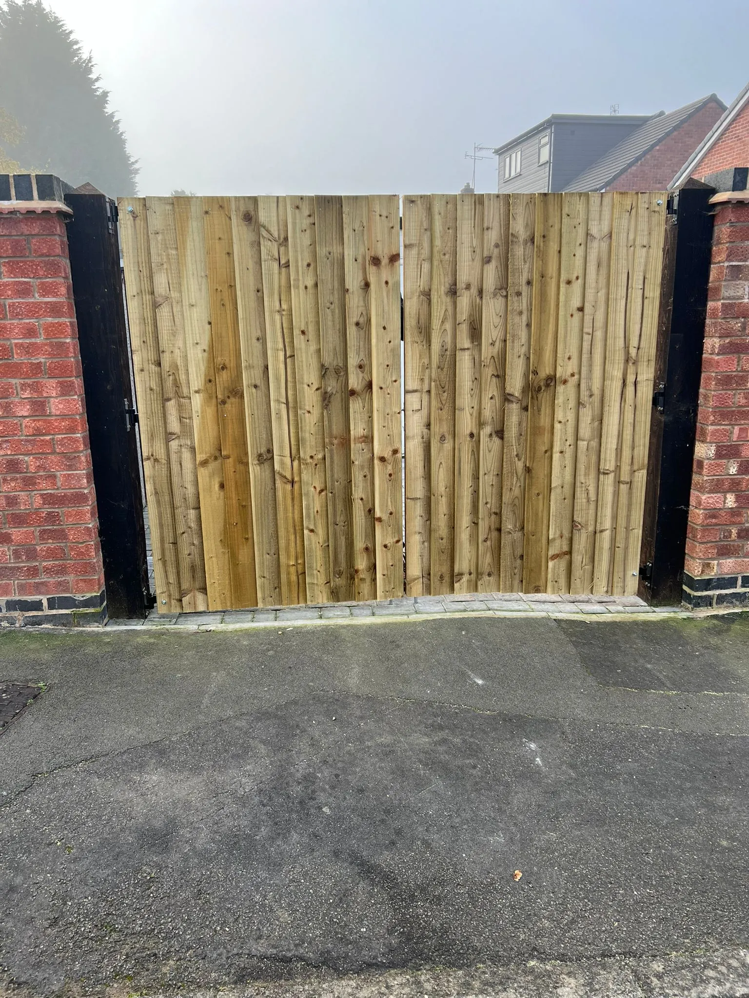 Newly installed wooden double gate with vertical timber slats and brick pillars, leading to a property entrance.