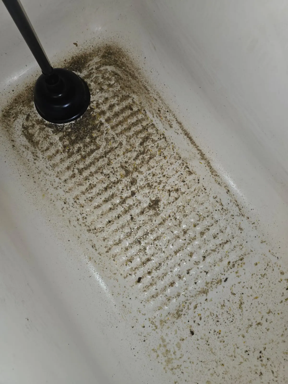 A heavily soiled blocked bathtub with a plunger highlighting a domestic drainage emergency