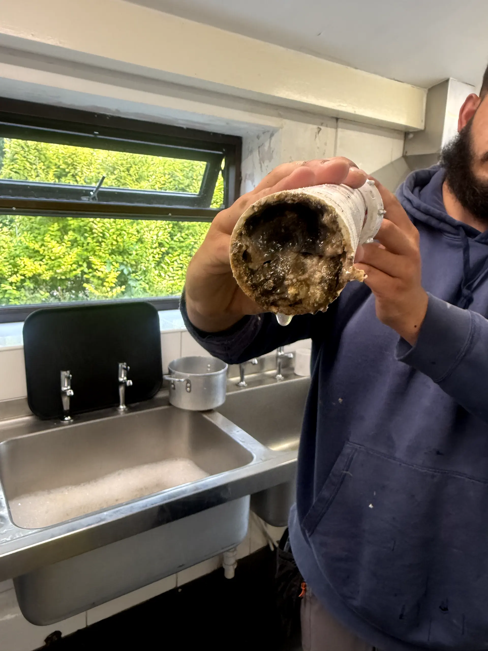 A severely blocked drain pipe being inspected by a WGS Services drainage engineer in a commercial kitchen