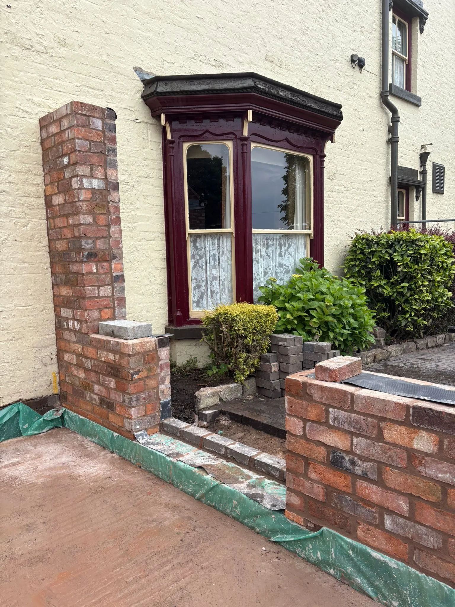 New brick walls under construction for a home extension, with a green damp-proof membrane visible at the base.