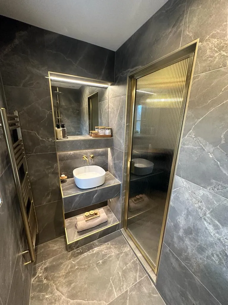 Luxury master bathroom design and installation in Plymouth featuring dark marble tiles and gold fixtures by Sands & Vossen.