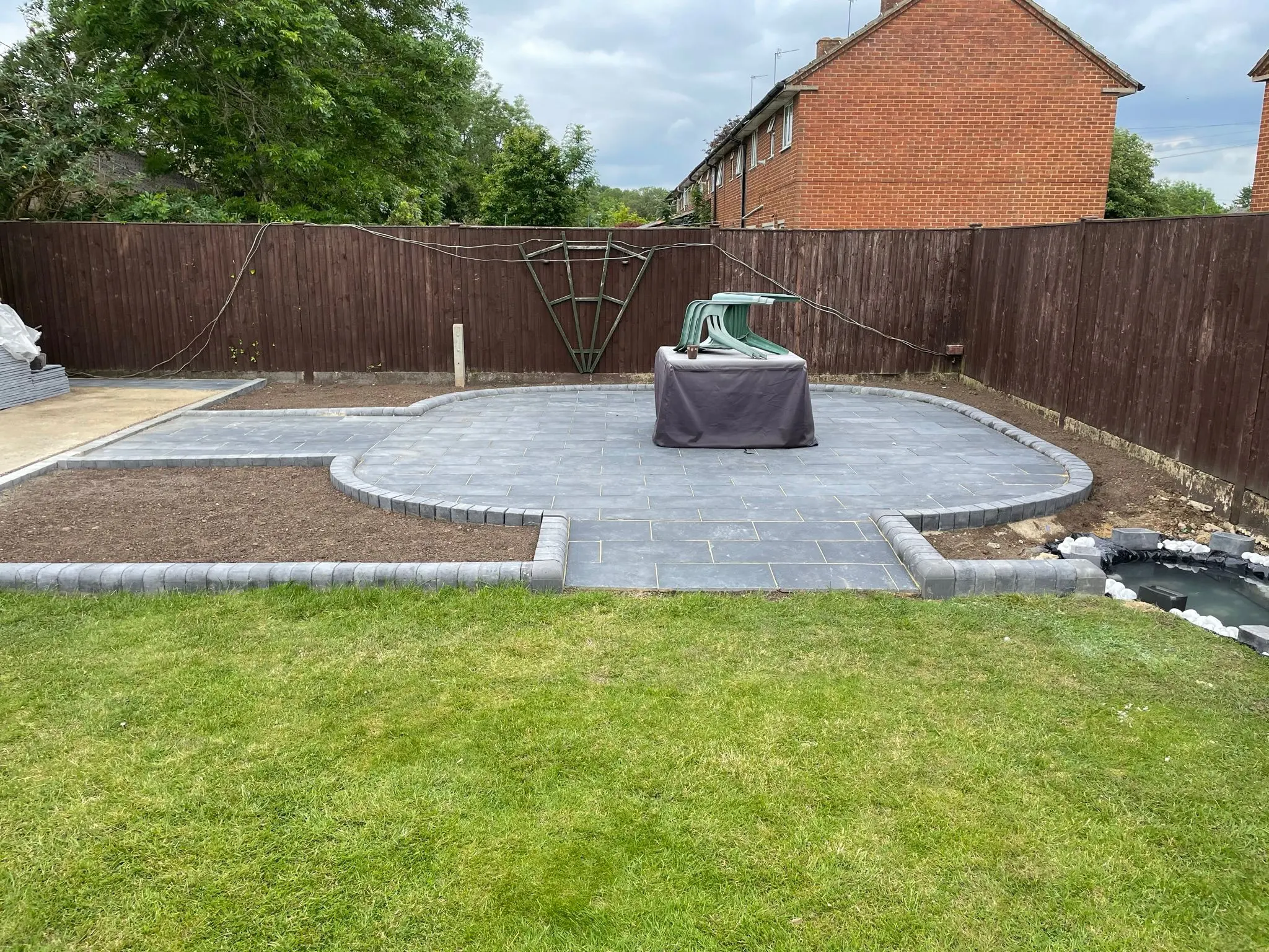 Newly laid bespoke grey patio with block paving edging in a residential garden