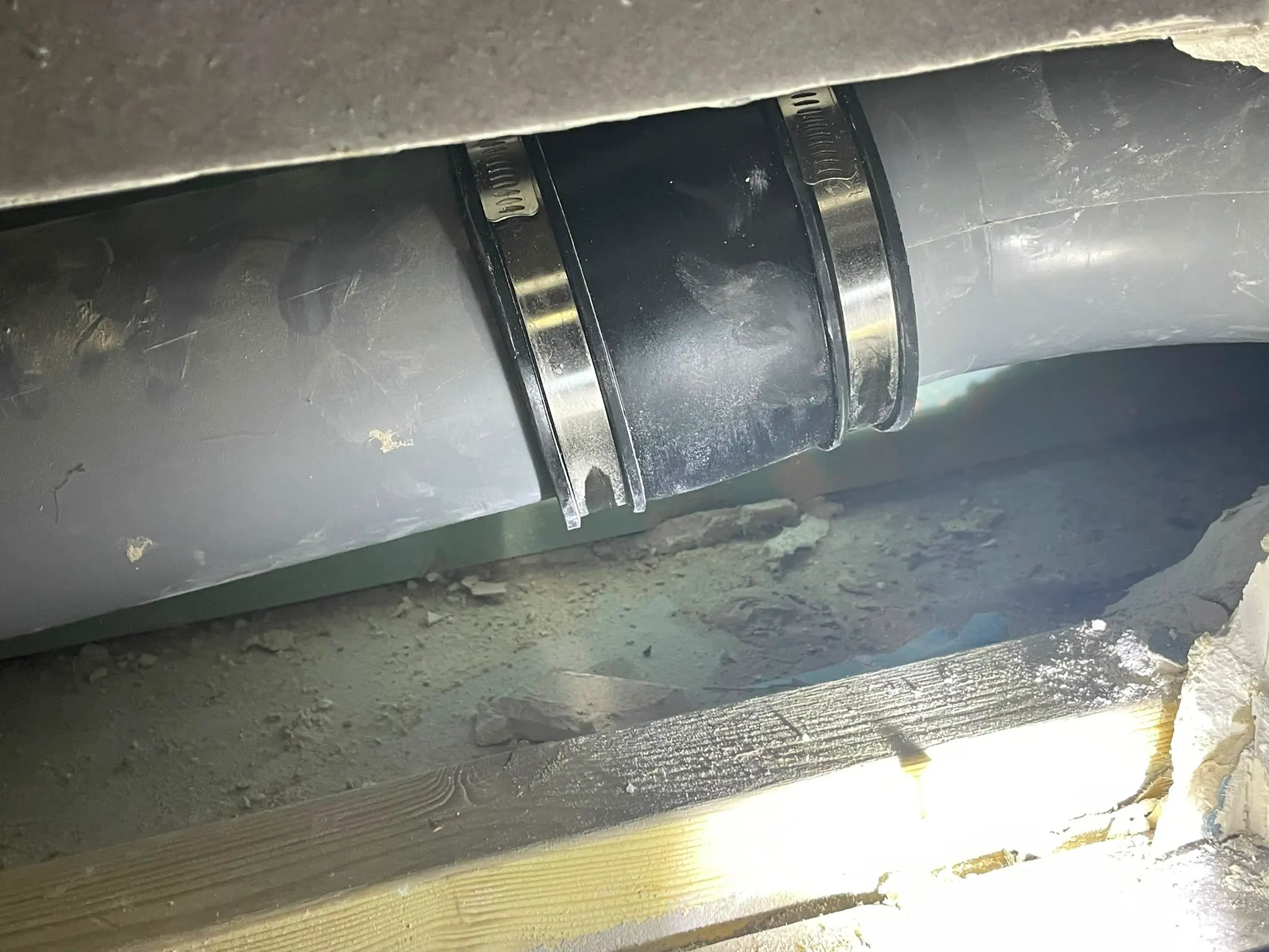 A repaired section of grey plastic pipework joined with a black flexible coupling and metal clamps