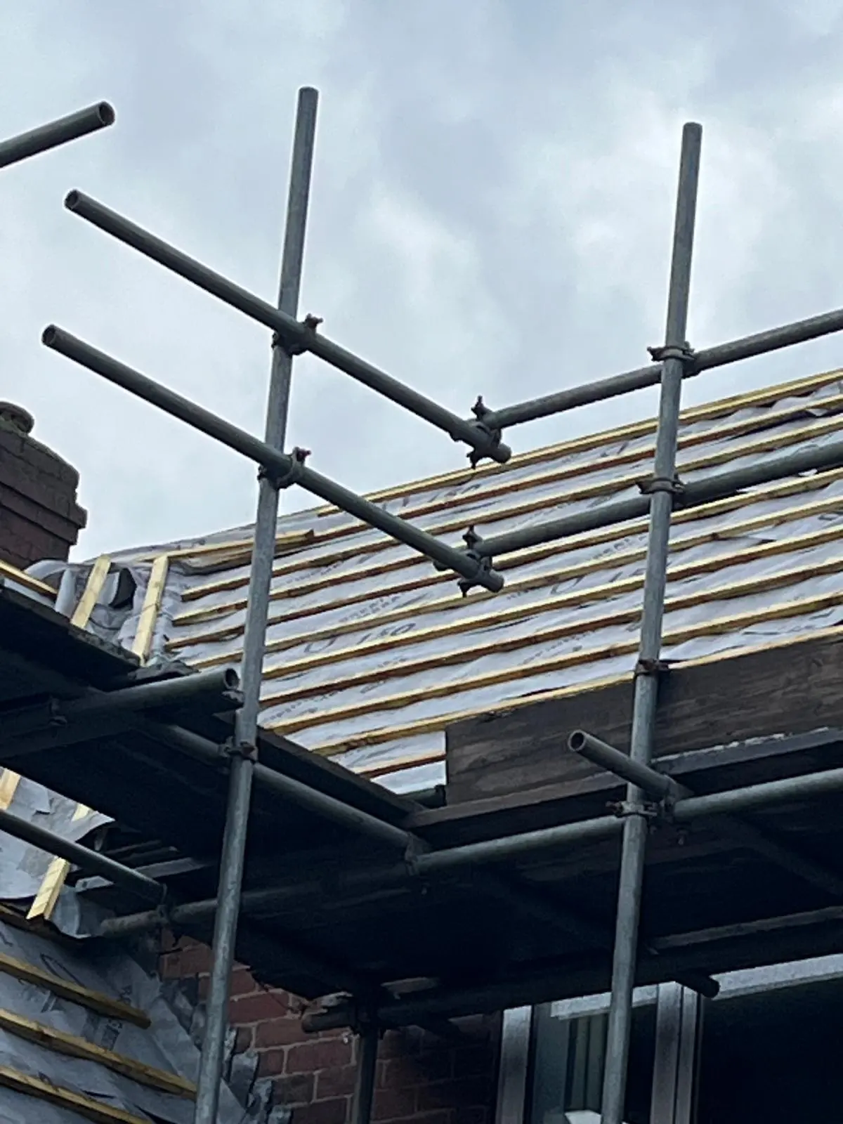 A pitched roof replacement in progress with new timber battens, waterproof underlay, and scaffolding set up