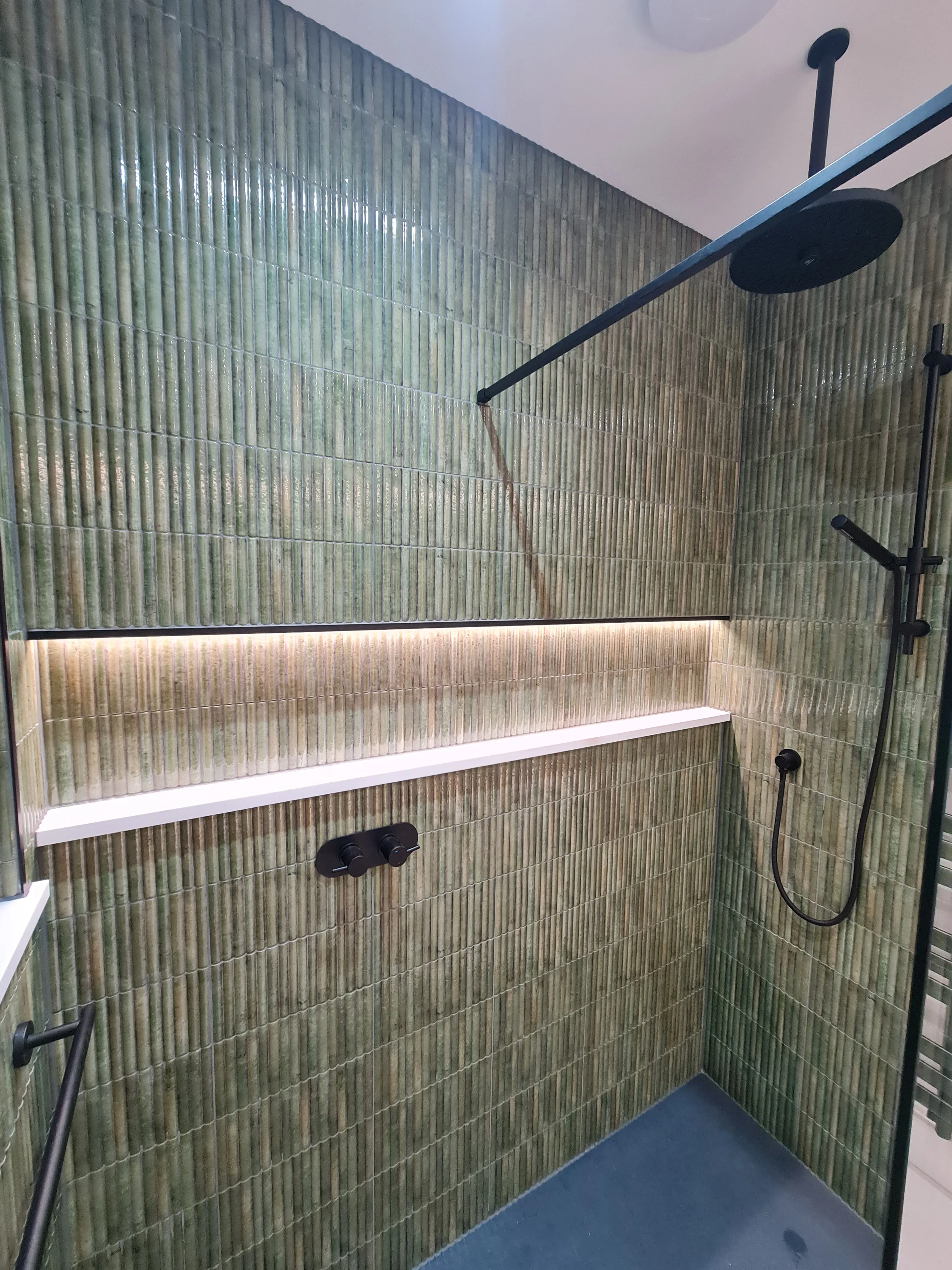 High-end walk-in shower with green kit-kat tiling, matt black shower head, and illuminated recessed shelf installed by Sands & Vossen in Plymouth.