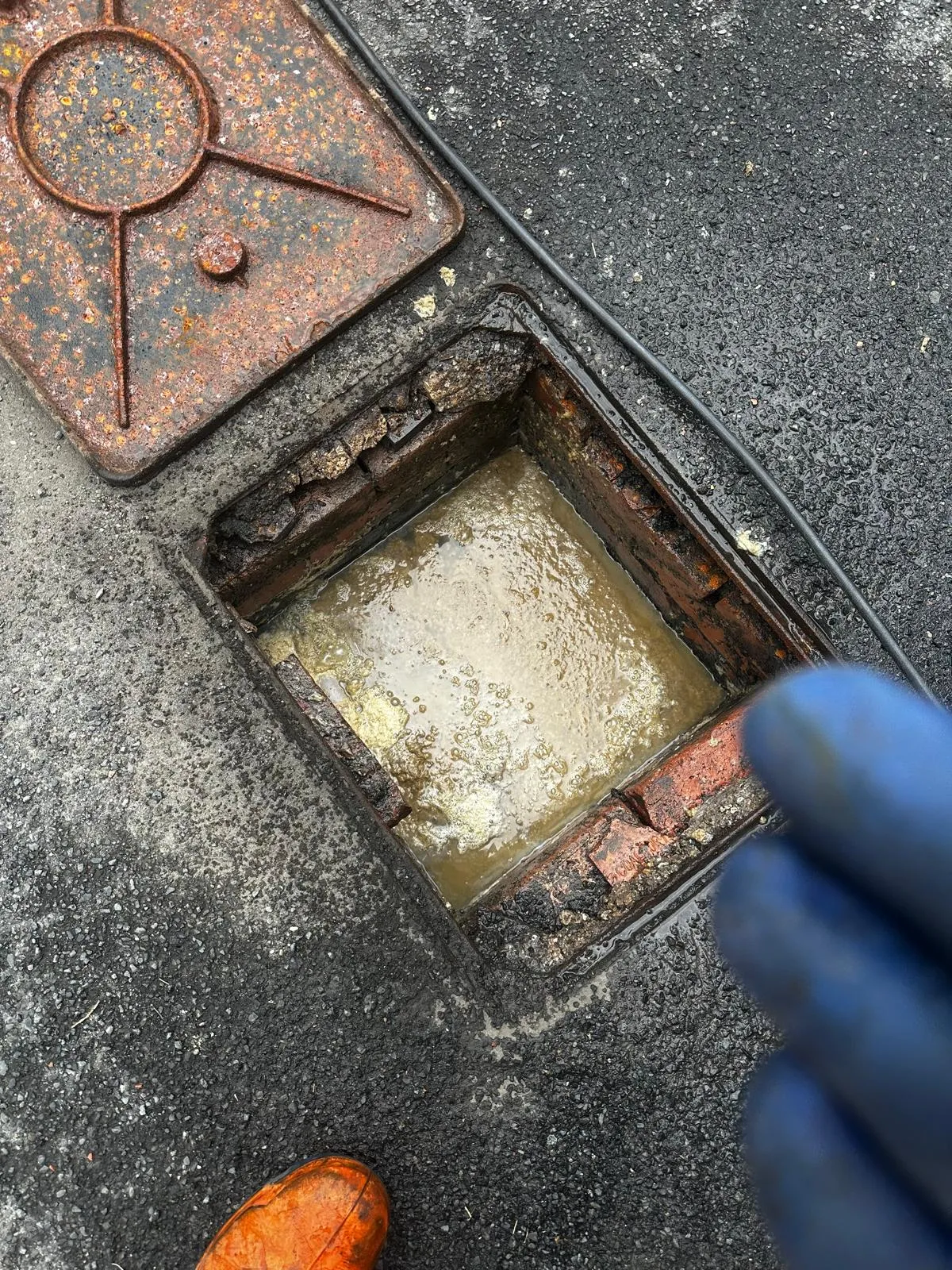 An image showing a blocked outdoor drain or inspection chamber overflowing with dirty water.