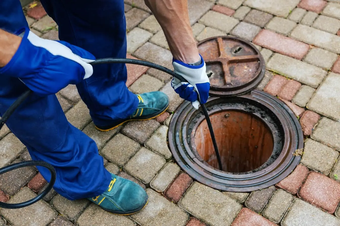 Drain Medics engineer performing emergency drain unblocking or a CCTV drain survey using specialist cable equipment in an open manhole.