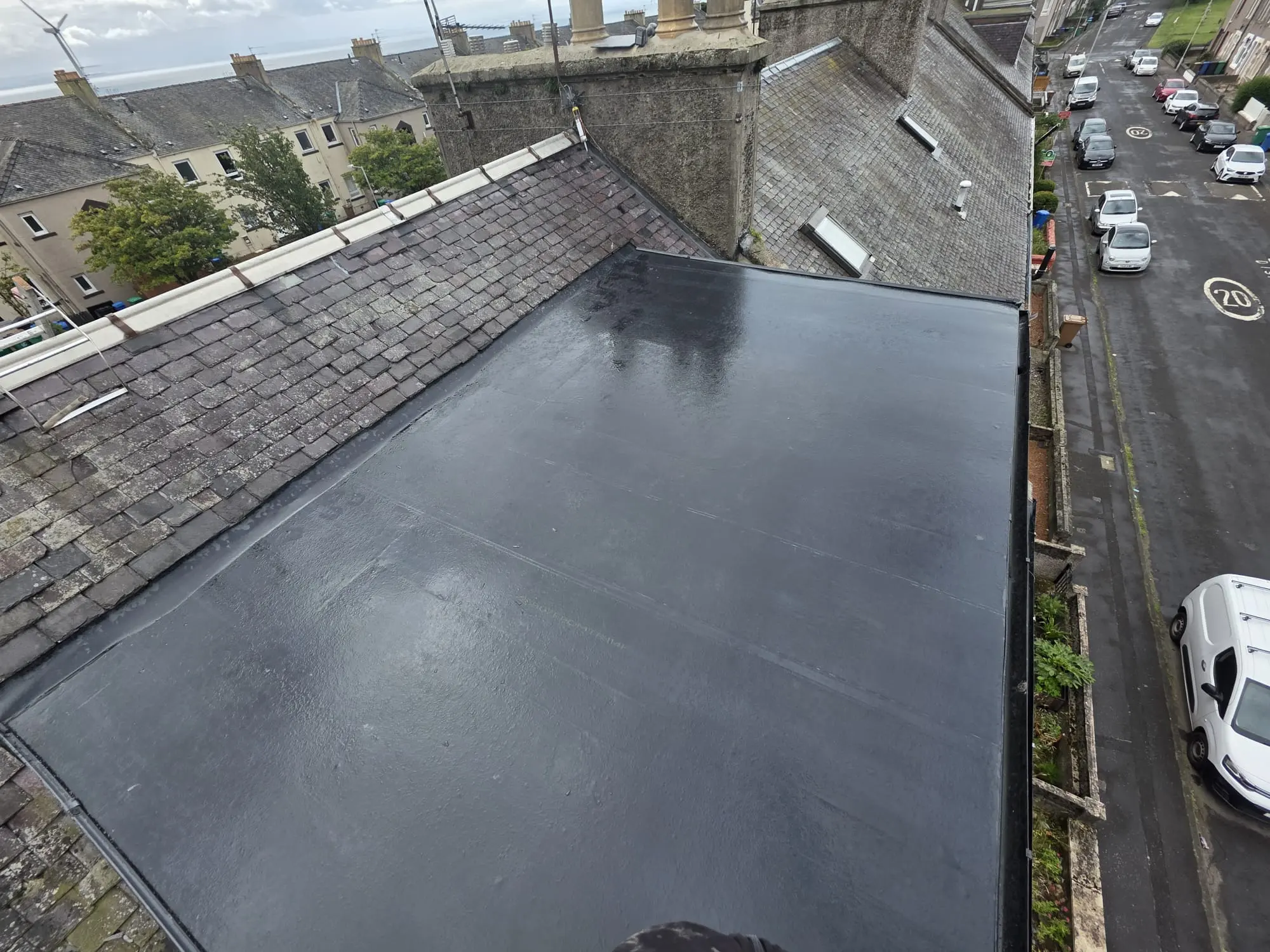 A newly installed black flat roof connecting to a pitched slate roof