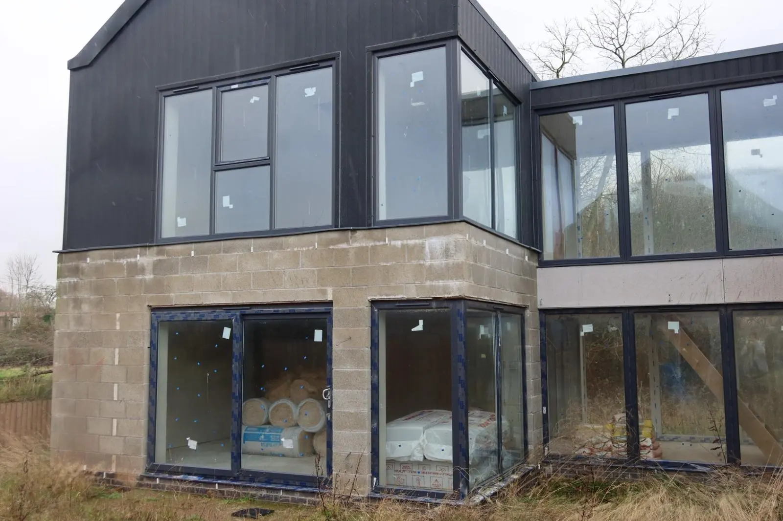 Modern home under construction showing exposed concrete blocks ready for external wall insulation or rendering, with thermal insulation rolls stored inside.