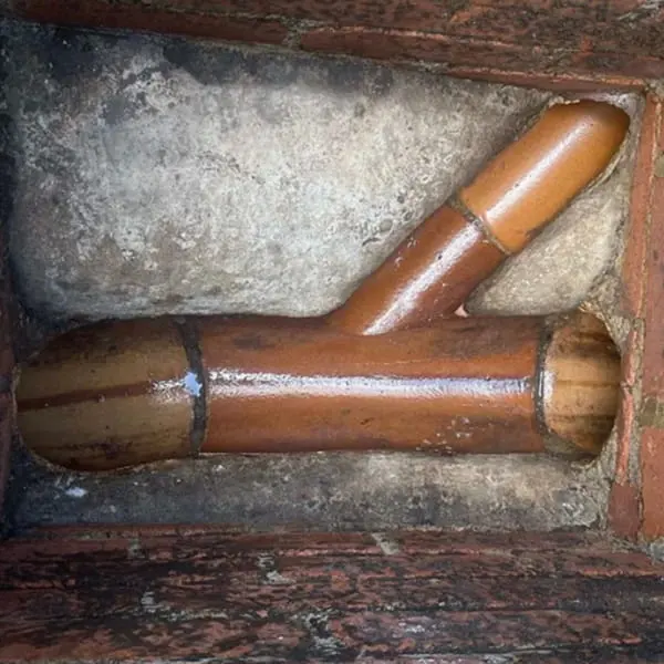 Traditional Y-shaped clay drain pipe junction located inside a brick inspection chamber