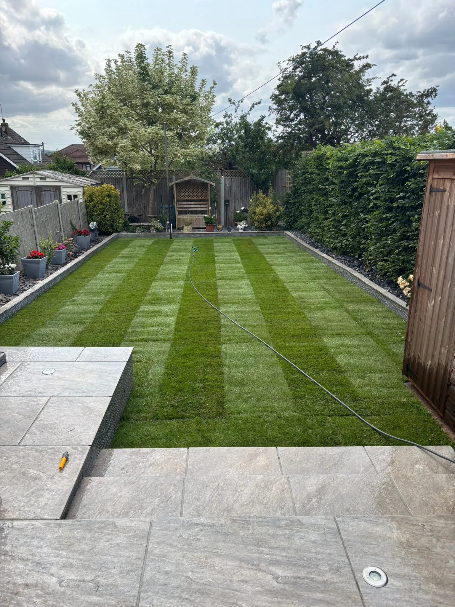 A freshly laid striped turf lawn and porcelain patio in a landscaped back garden in Essex