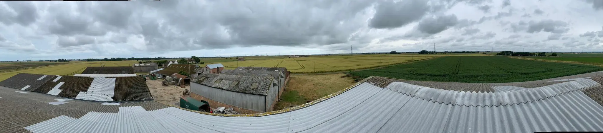 Panoramic view over the roofs of multiple agricultural farm sheds and buildings surrounded by fields