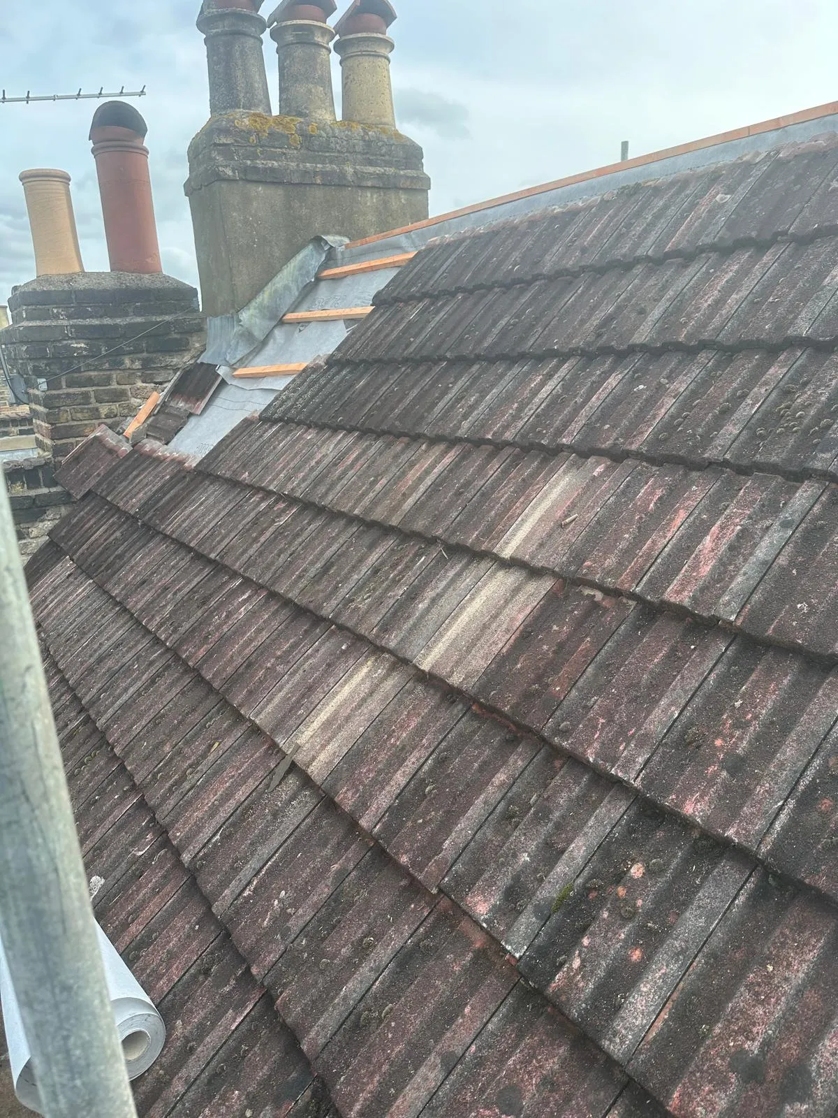 Professional roof tile repairs in progress showing new battens and lead flashing next to a chimney.