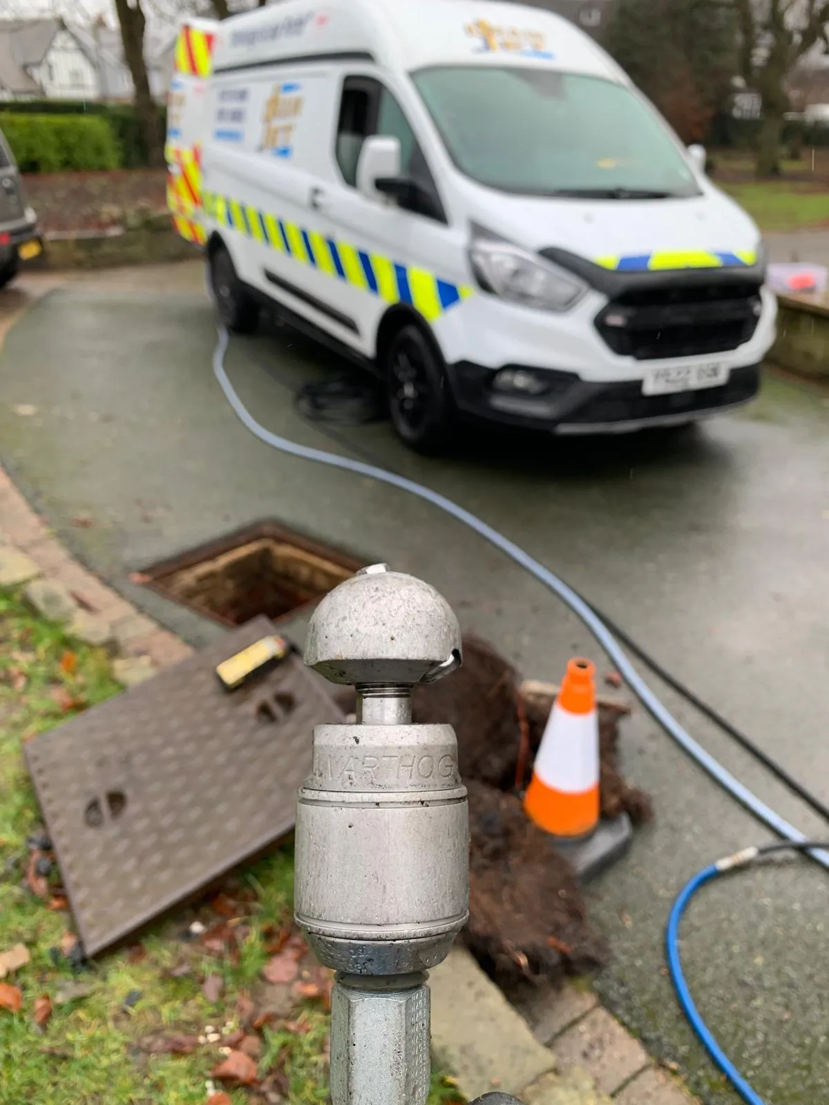 High-pressure rotary nozzle used for drain root removal with a service van on a residential driveway.