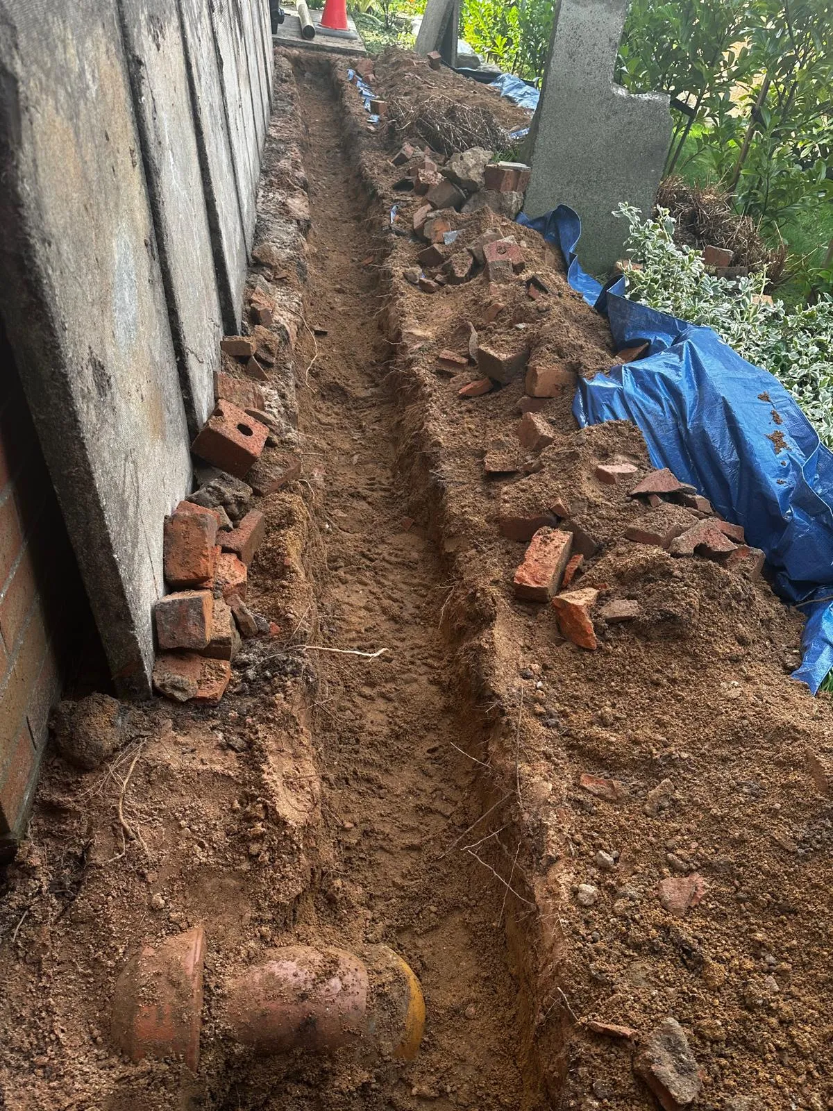 An excavated trench showing old clay drainage pipes for repair or installation.