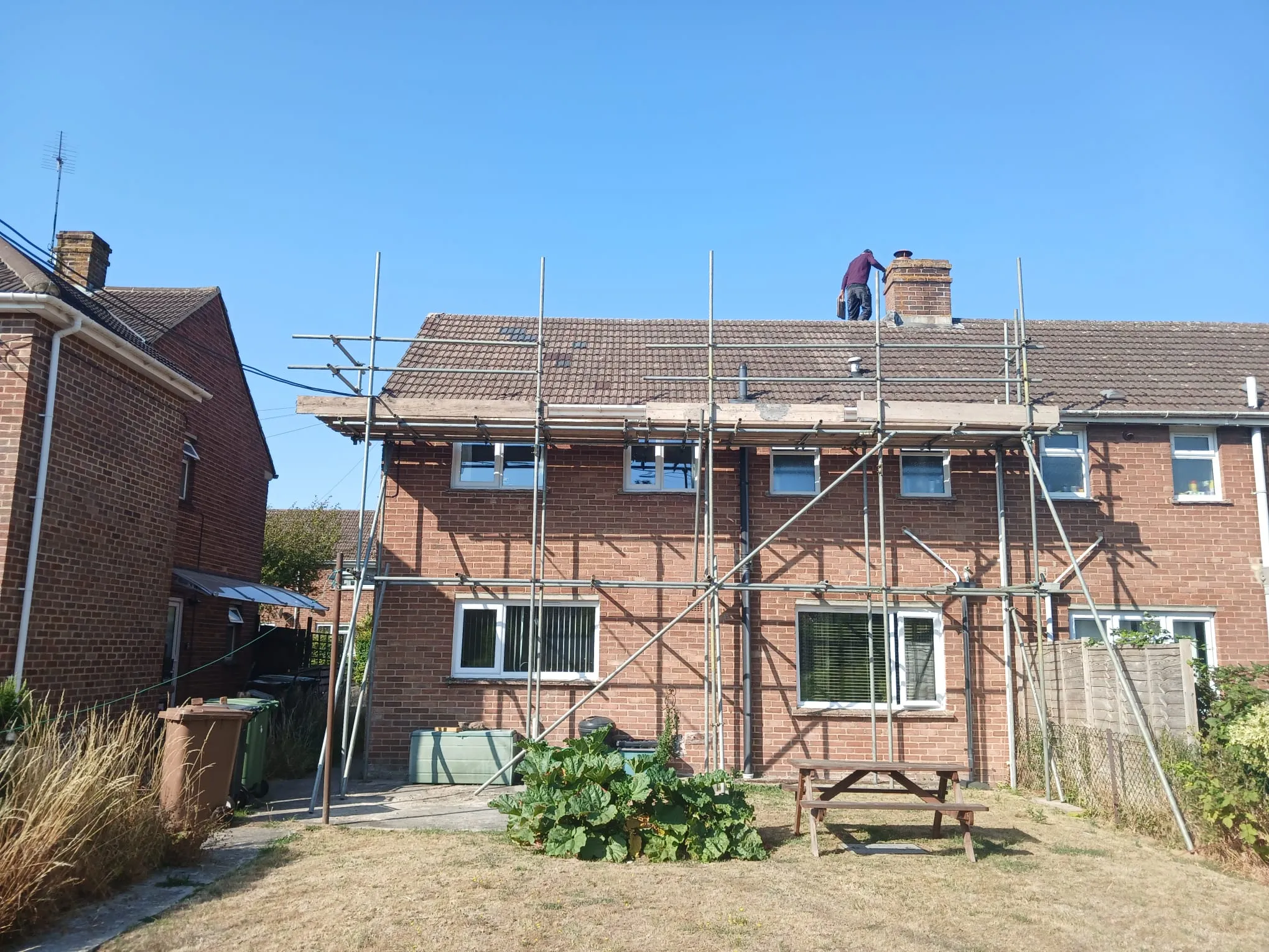 Roofer carrying out chimney stack repairs and roofline maintenance from scaffolding on a tiled residential property
