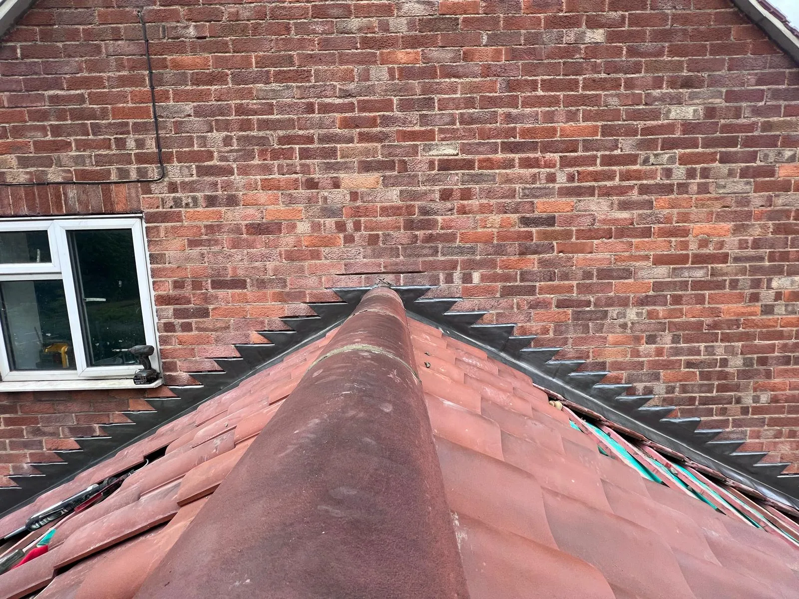 Stepped lead flashing where a terracotta-tiled pitched roof meets a brick wall, highlighting expert leadwork.
