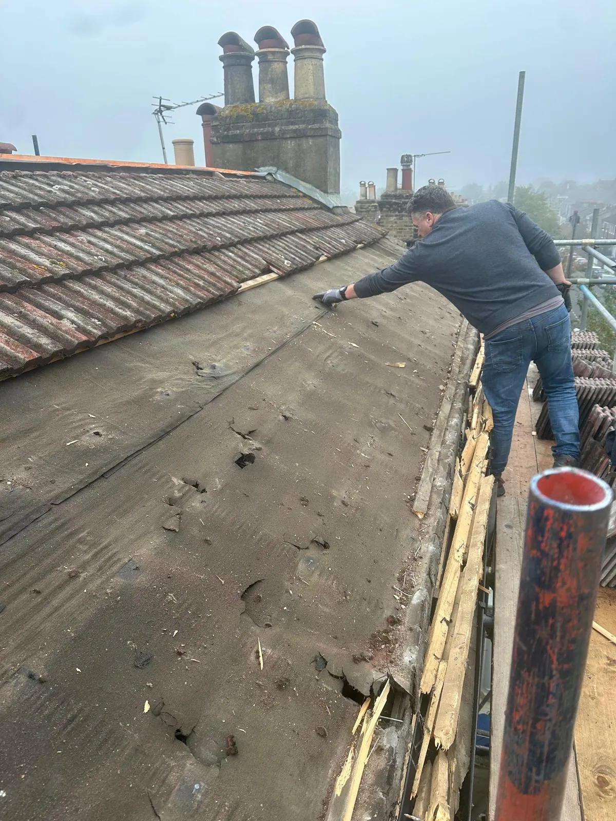 Professional roofer inspecting damaged roof underlayment and torn felt during a roof repair project in West Malling, Kent.