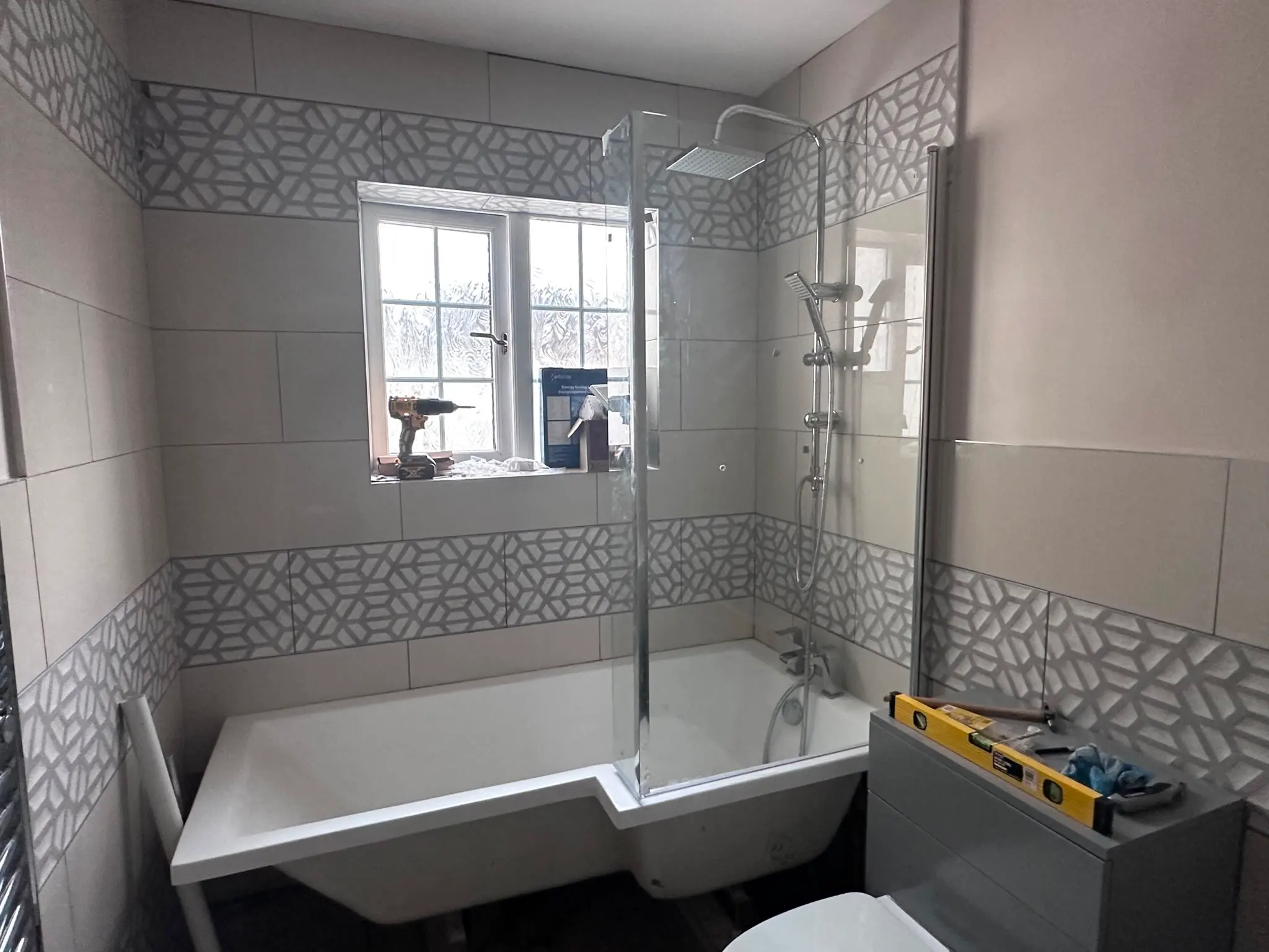 Newly installed modern bathroom with bathtub, shower screen, and geometric wall tiles in Snodland, Kent, fitted by JMA Plumbing & Heating.