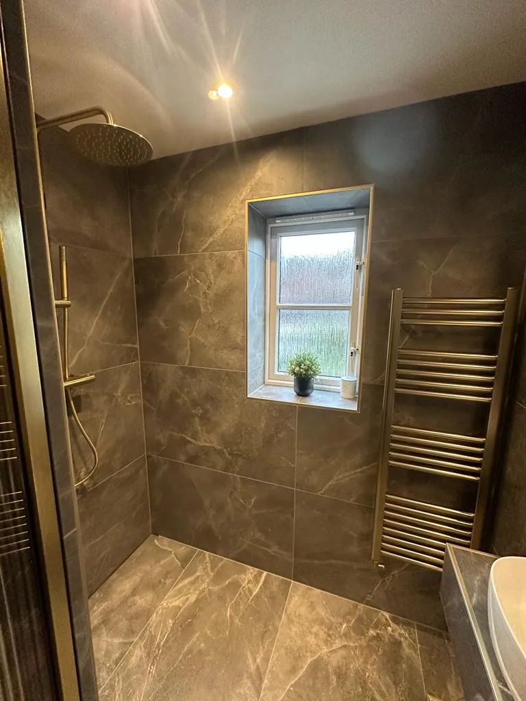 Luxury walk-in shower installation in Plymouth featuring grey marble tiles and brushed gold fixtures by Sands & Vossen.