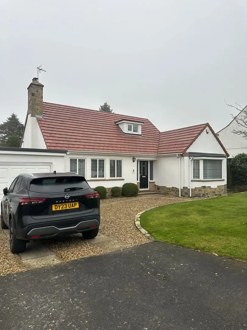 A white house with a new red tiled roof and a black car parked on a gravel driveway in Otley, Leeds