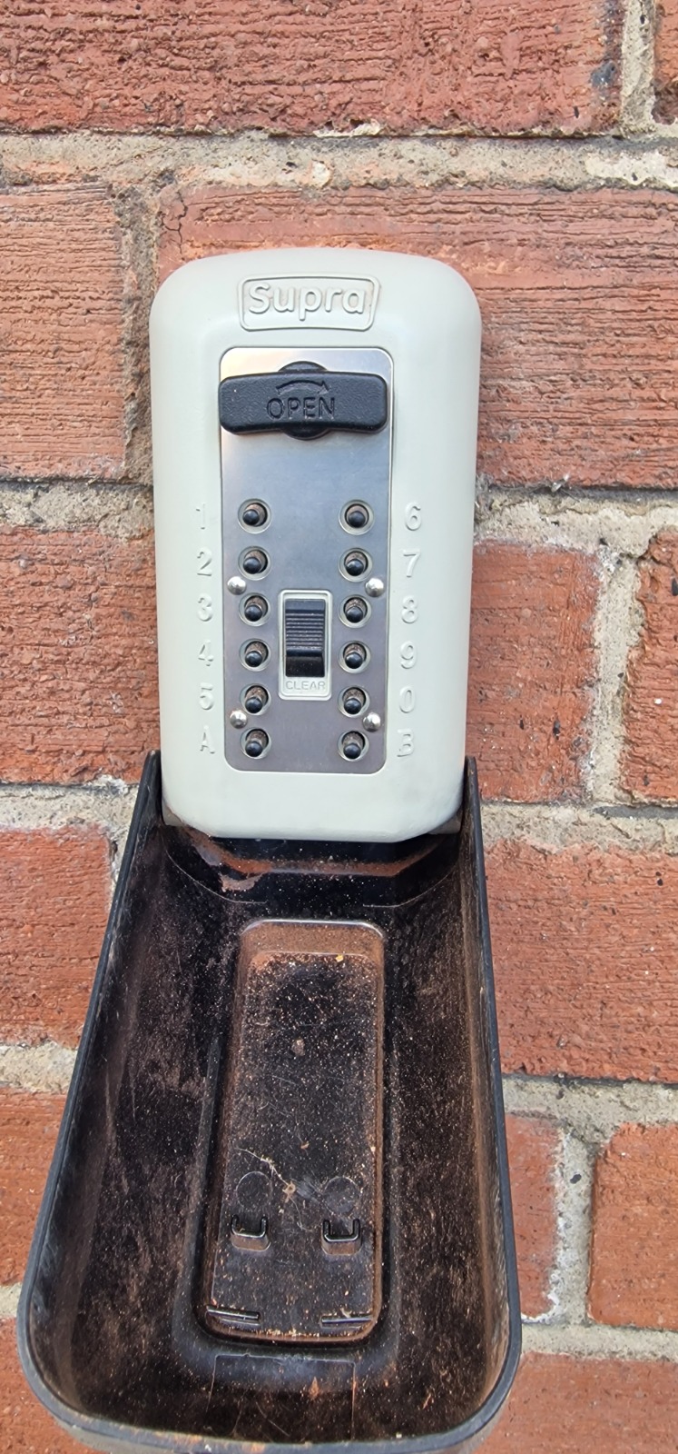 A Supra key safe box mounted on an external brick wall with the cover open.