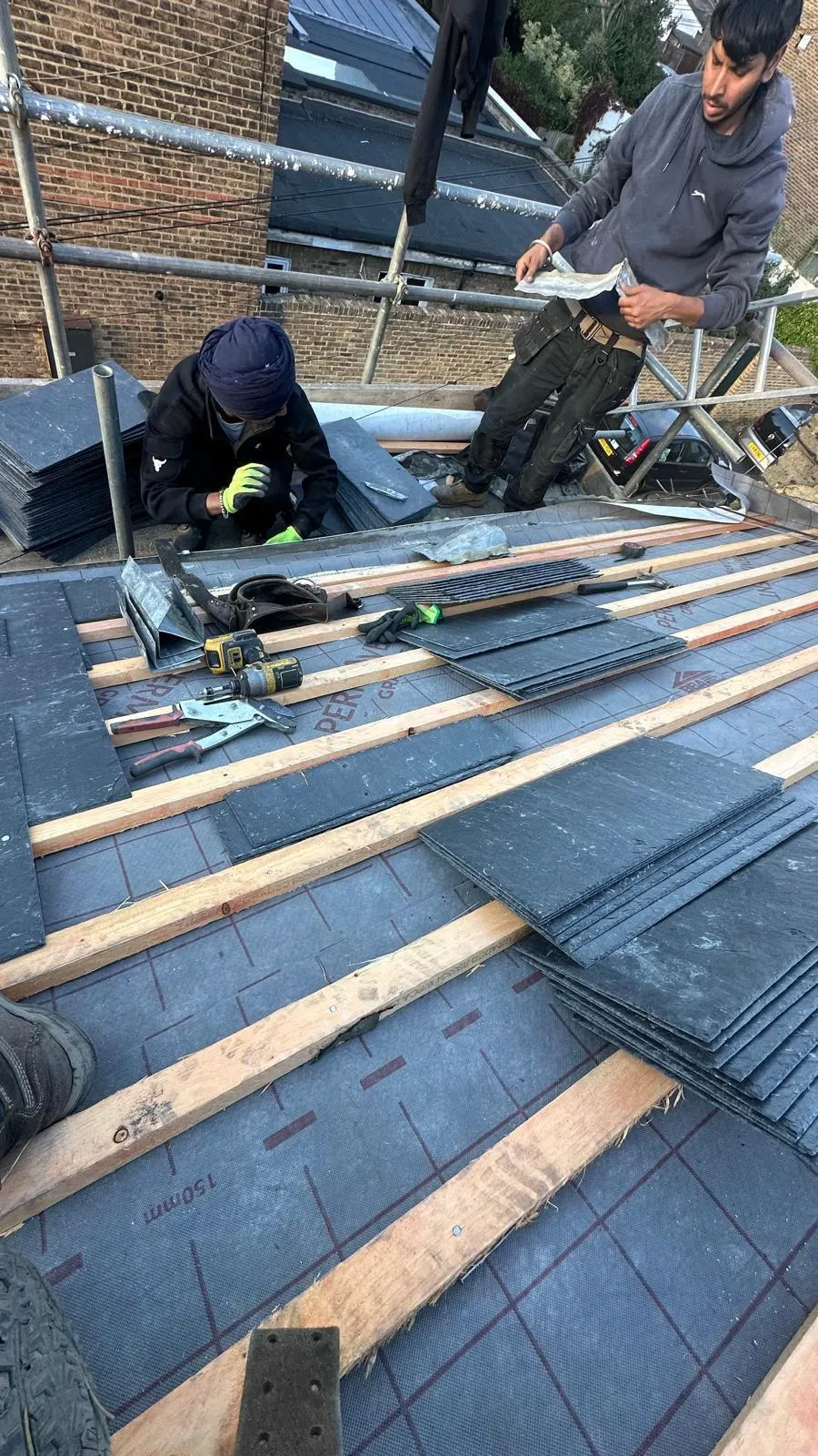 Roofing contractors laying natural slate tiles and fitting battens on a pitched roof