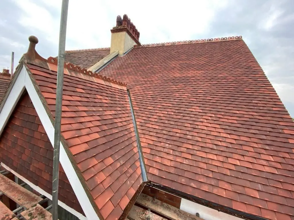 A close-up view of a newly installed pitched roof featuring red terracotta tiles and a traditional chimney stack, with scaffolding visible.