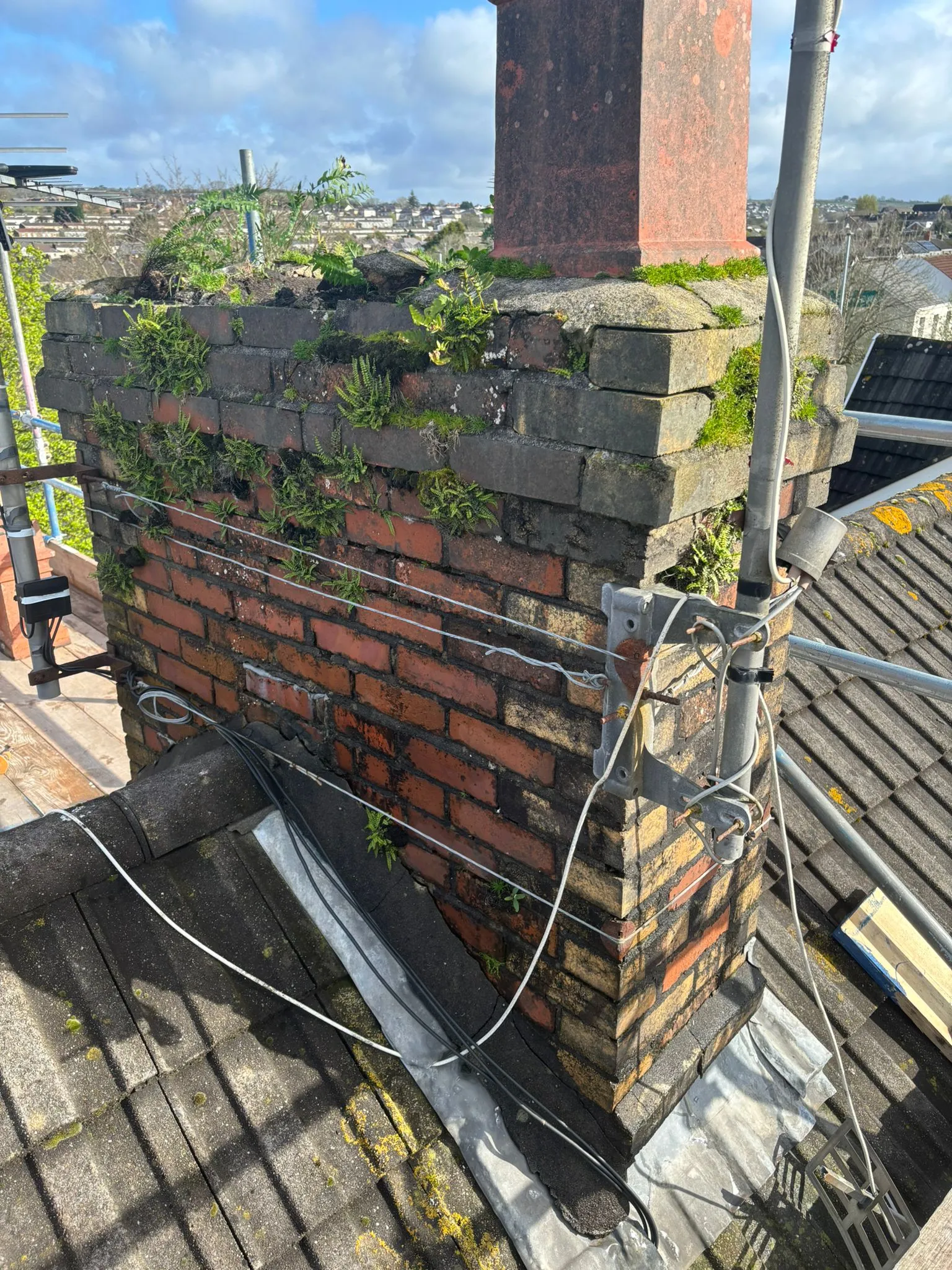 A weathered brick chimney in need of repointing and repair with vegetation growing out of the mortar.