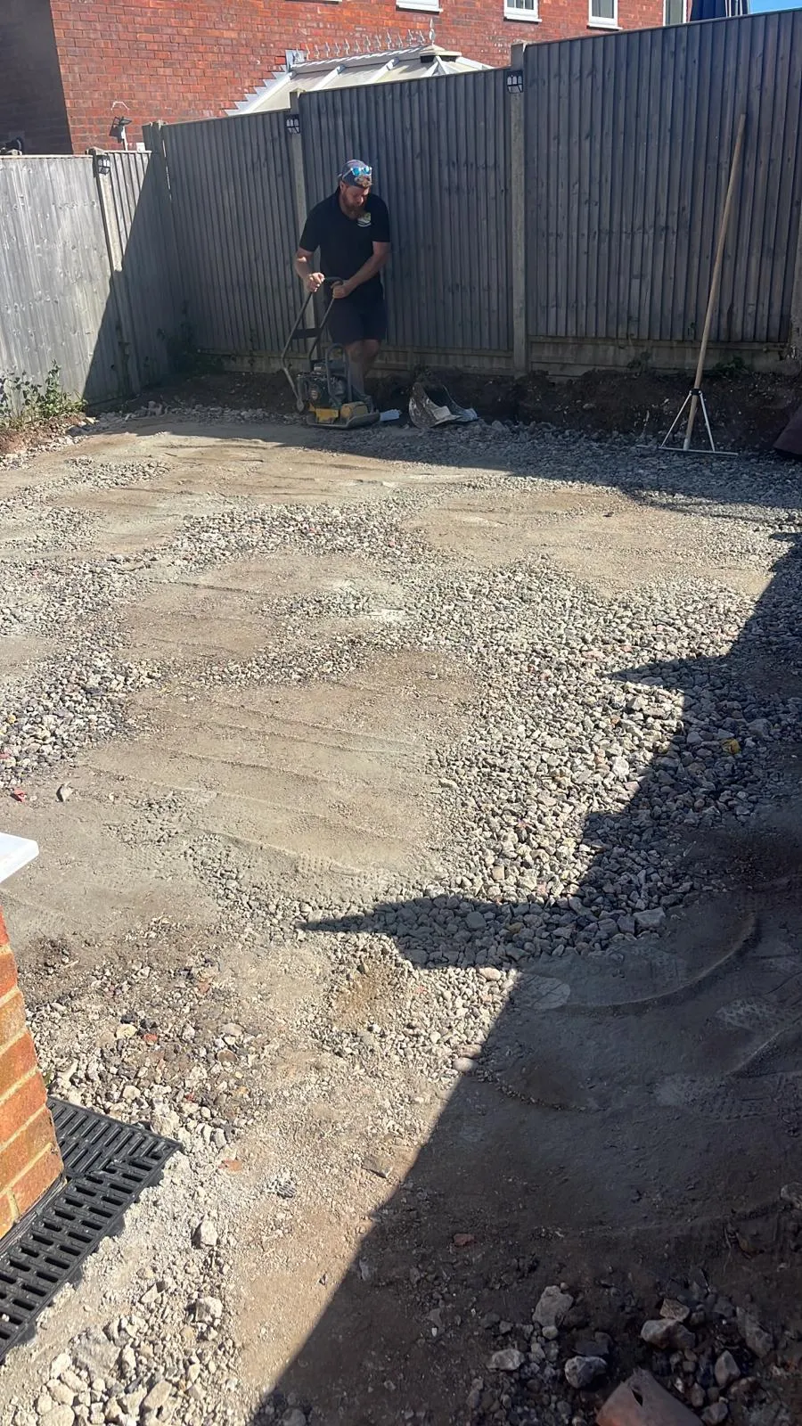 Groundworker compacting a driveway sub-base with a wacker plate, preparing the ground for a new surface. Shows essential groundwork for durable driveways.