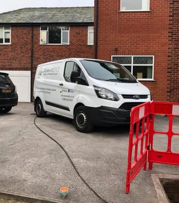 Drain Medics company van attending a residential drain unblocking call-out with safety barriers around an open manhole