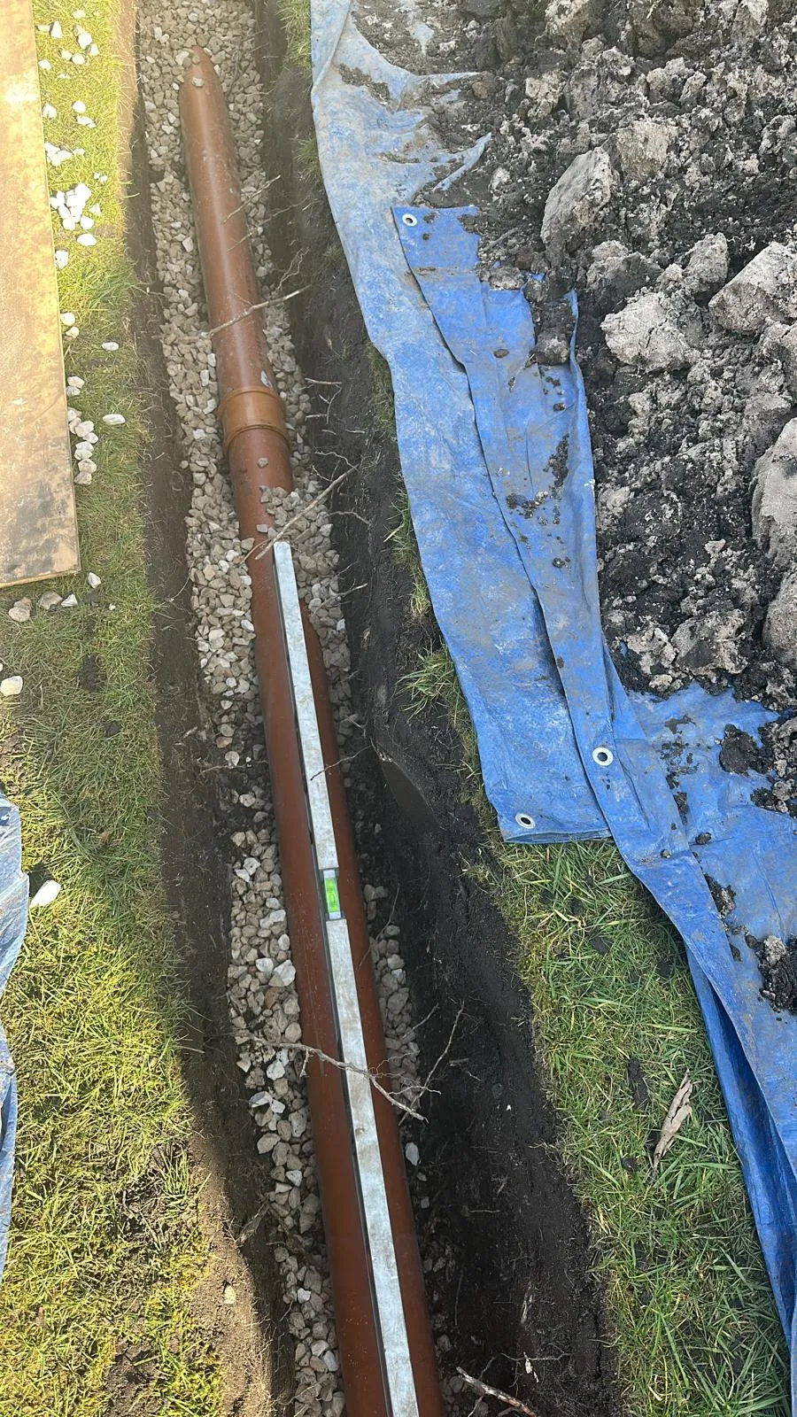 Drainage pipe being installed in a trench, showing a spirit level for correct gradient during drain installation or repair.