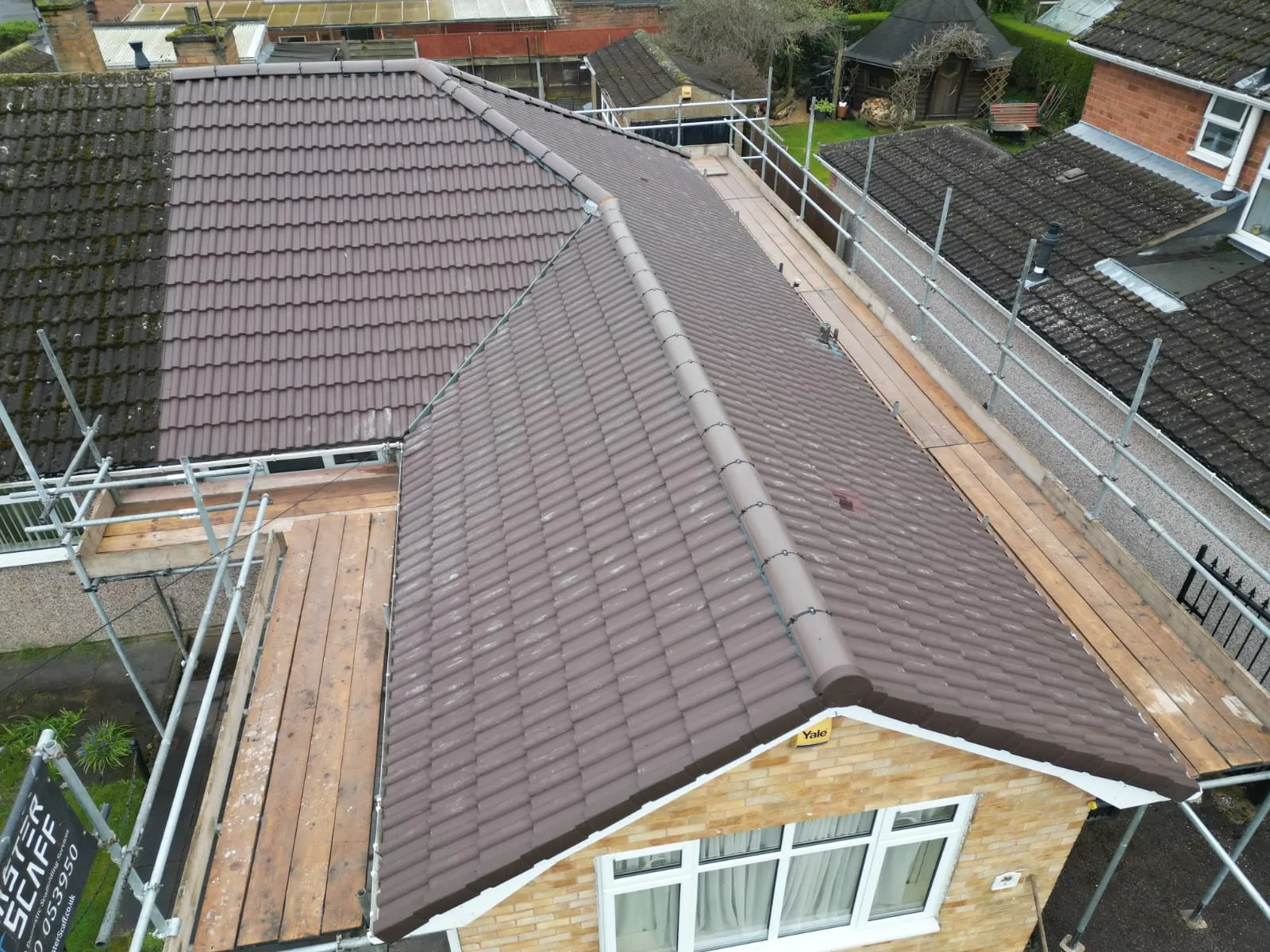 Before and after comparison of a roof during a re-tiling project, showing new brown tiles next to old, mossy roof tiles with scaffolding.