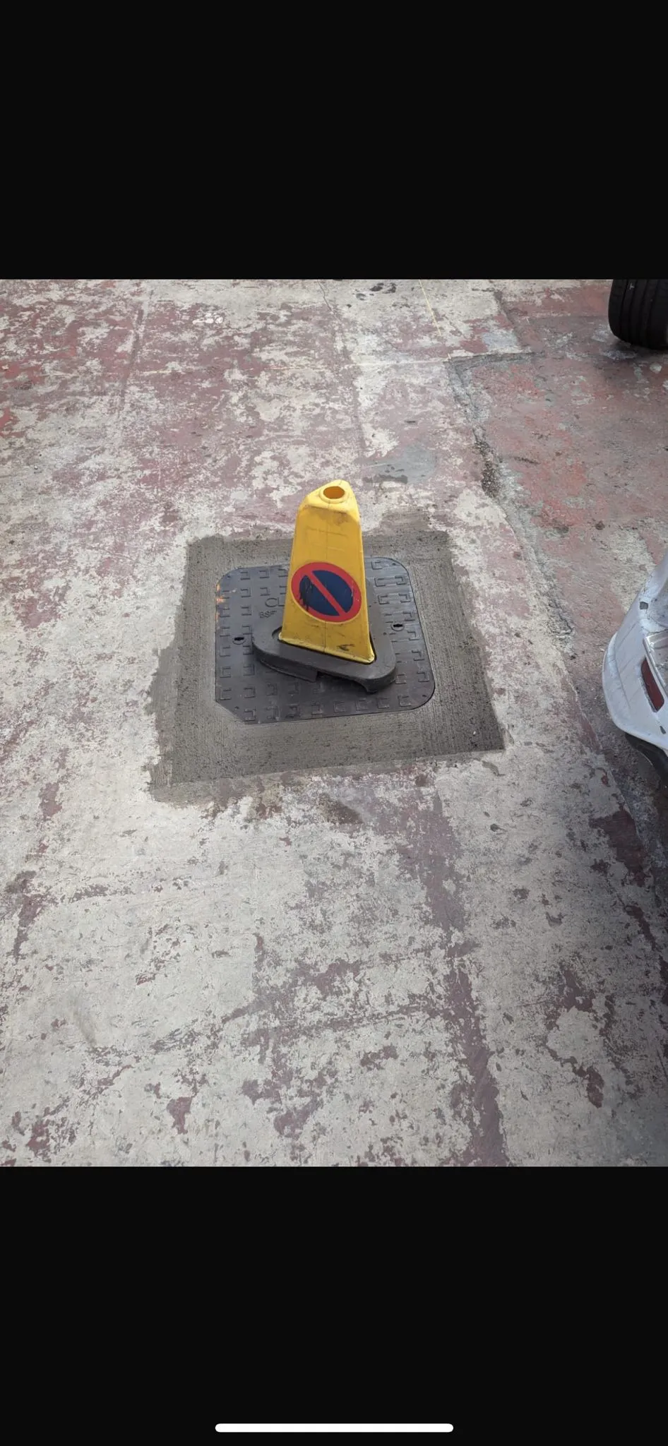 Yellow warning cone on a manhole cover, signifying active drainage work or drain inspection in progress.