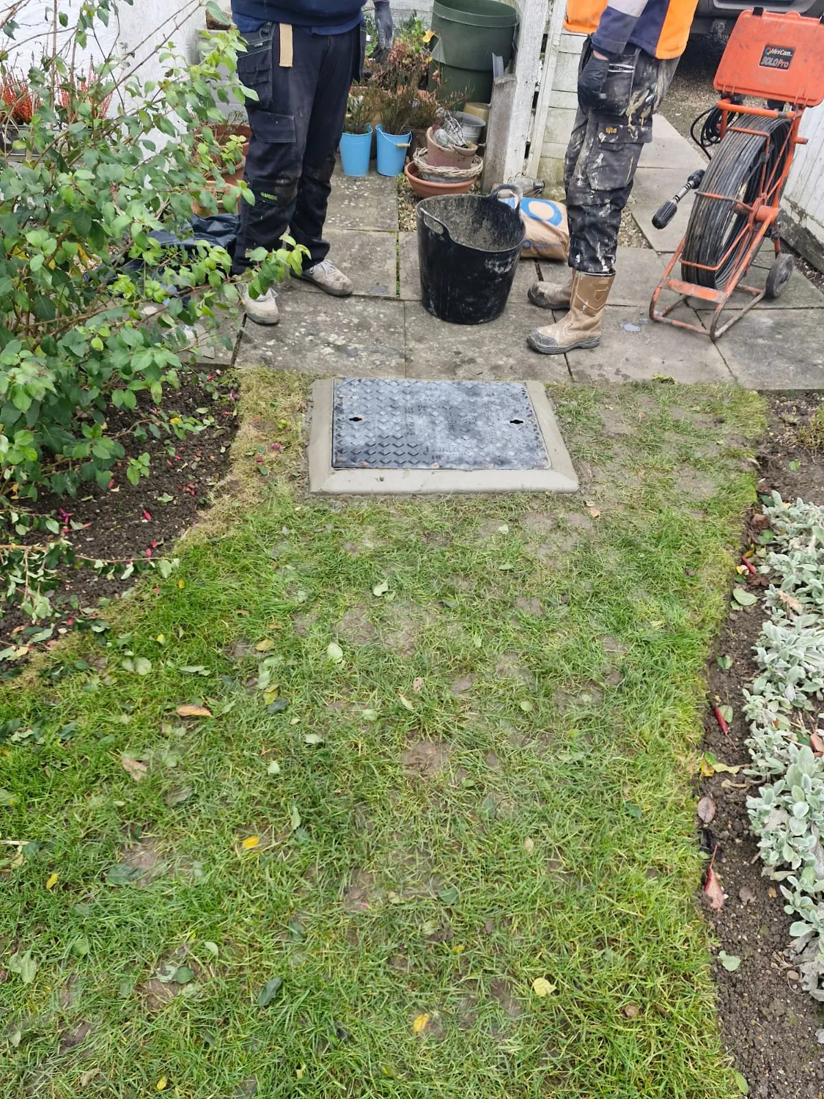 Drainage engineers completing a drain repair and manhole cover installation in a customer's garden.
