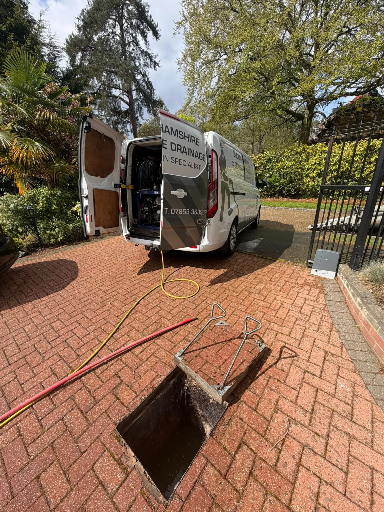 Professional drain unblocking service in progress with a Buckinghamshire & Berkshire Drainage van and high-pressure equipment on a residential driveway.