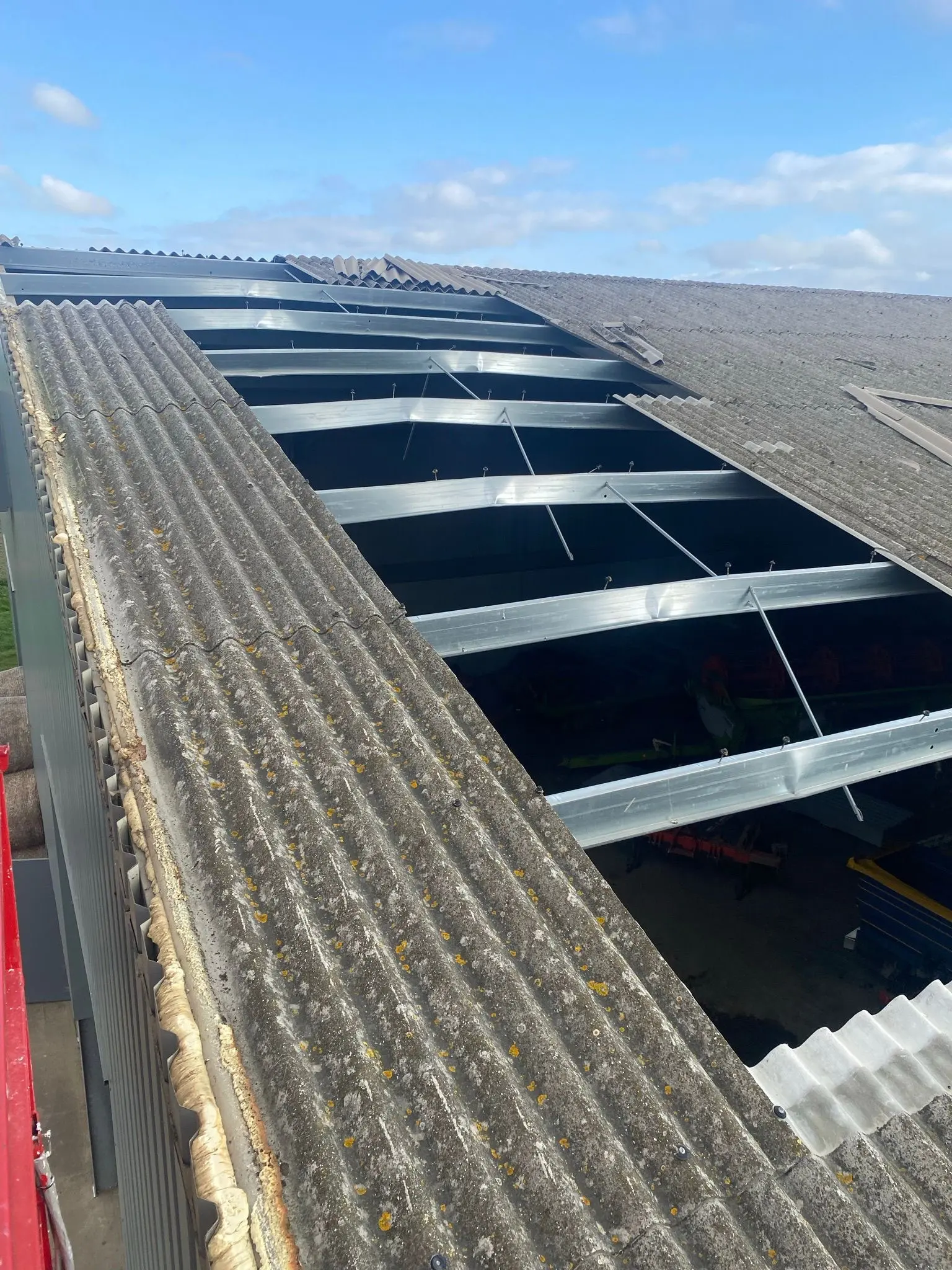 Storm damaged roof cladding repairs on an agricultural barn showing exposed steel purlins