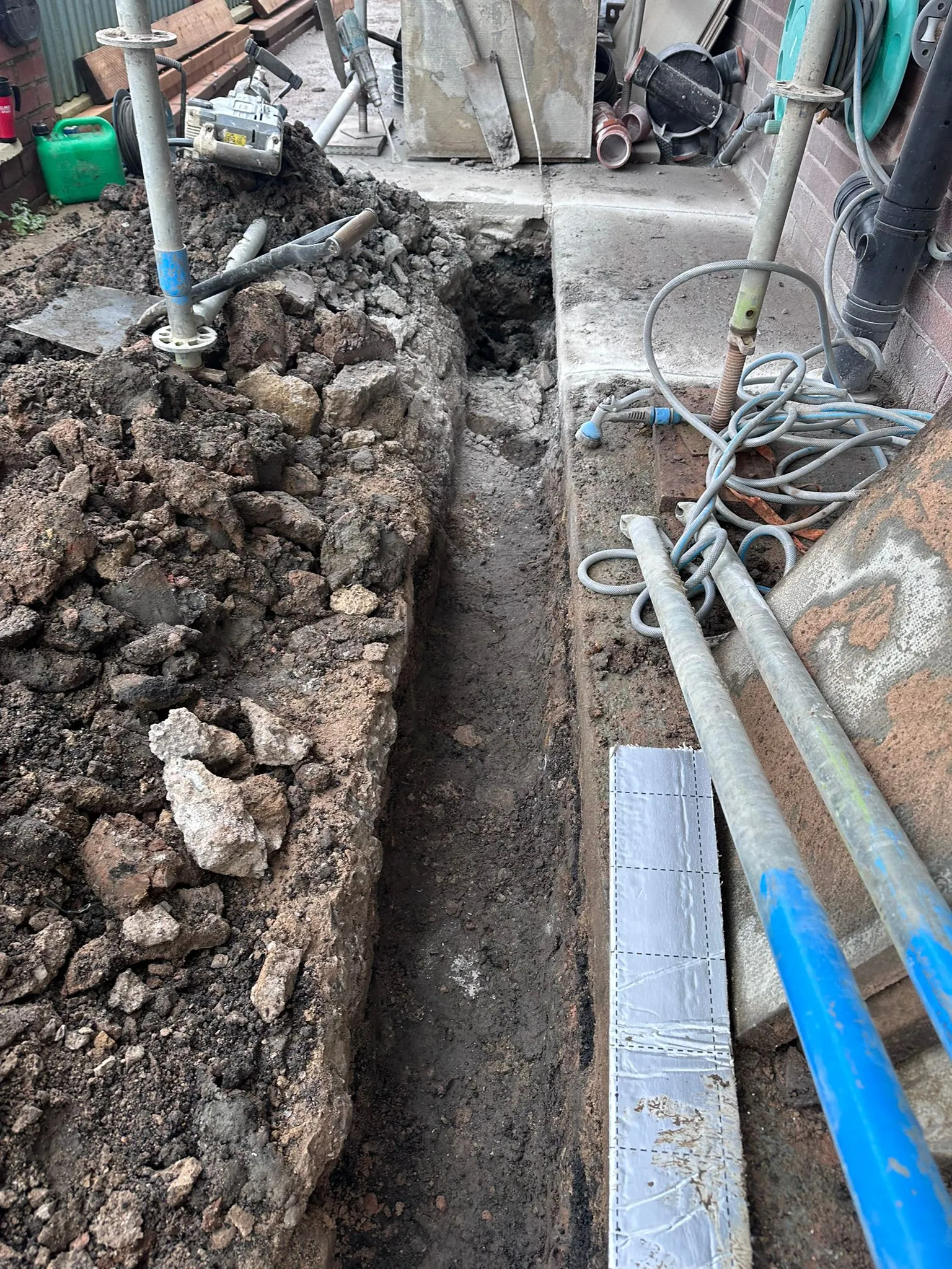 An excavated trench next to a house for drainage repair work in Macclesfield, showcasing expert excavation services.