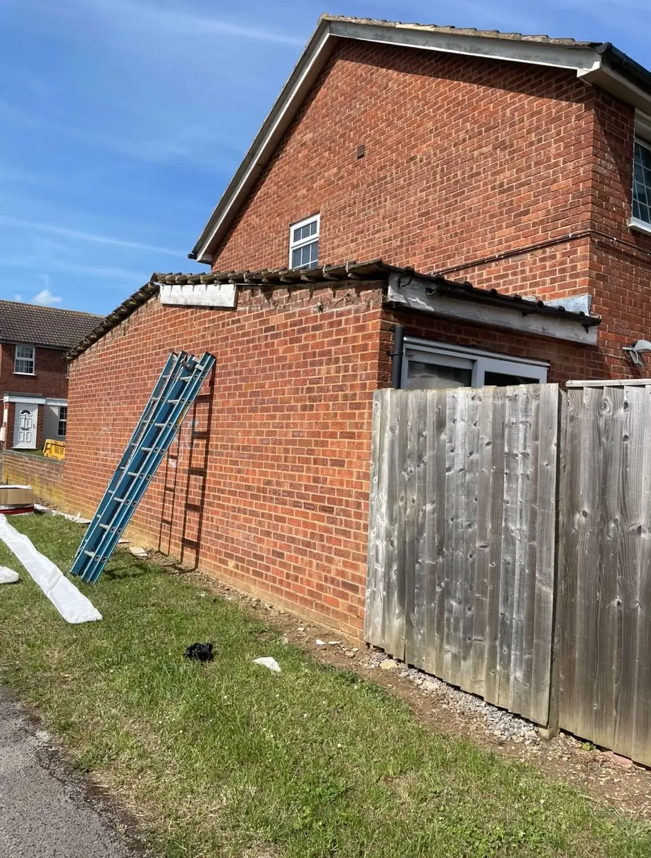 A blue ladder leaning against a brick property in Northampton during roofline, fascia, and soffit repair work.
