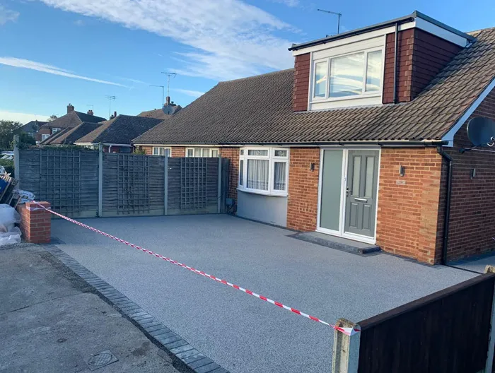 Newly completed light grey resin-bound driveway in front of a bungalow, featuring new block paving edging.