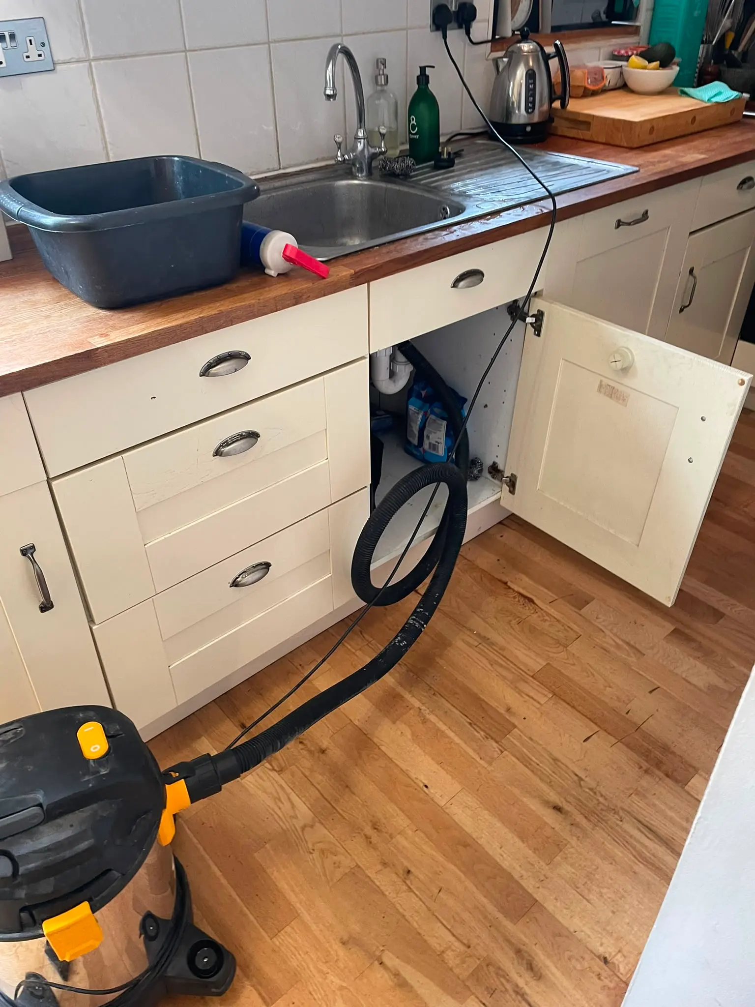 Plumbing repair in progress using a wet vacuum to unblock a kitchen sink drain.