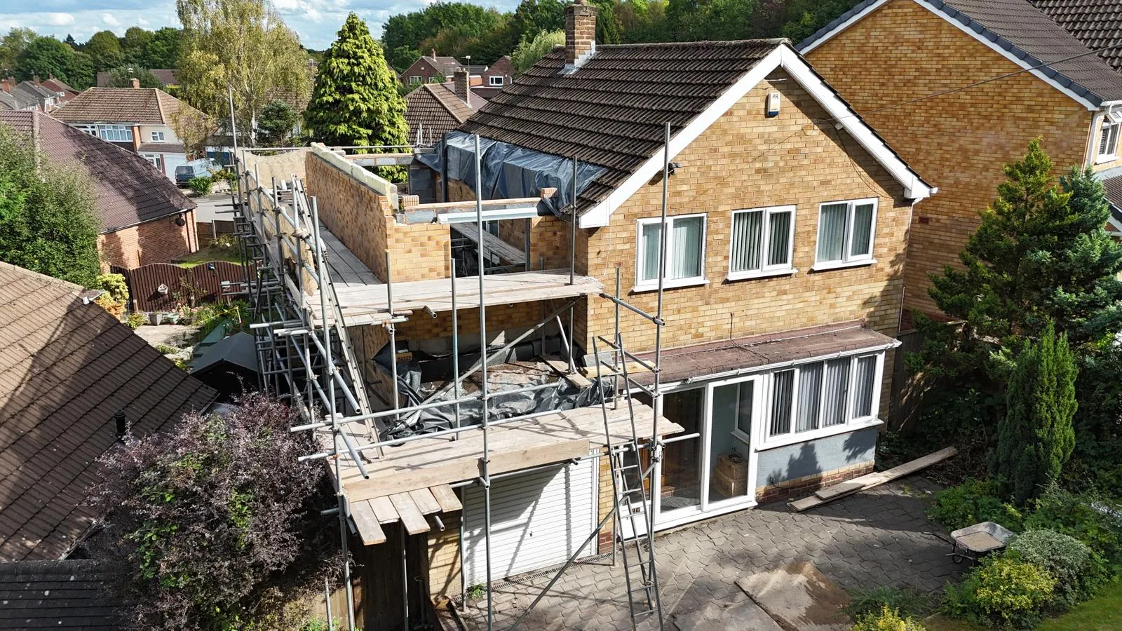 A house with new brick foundations and a prepared ground area for a single-storey rear extension under construction.