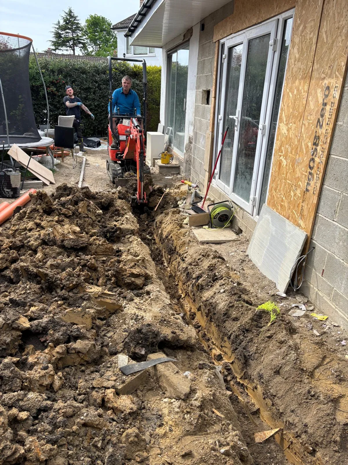 Drainage engineers using an excavator to dig a trench for drain repairs and installations at a home in Leeds.