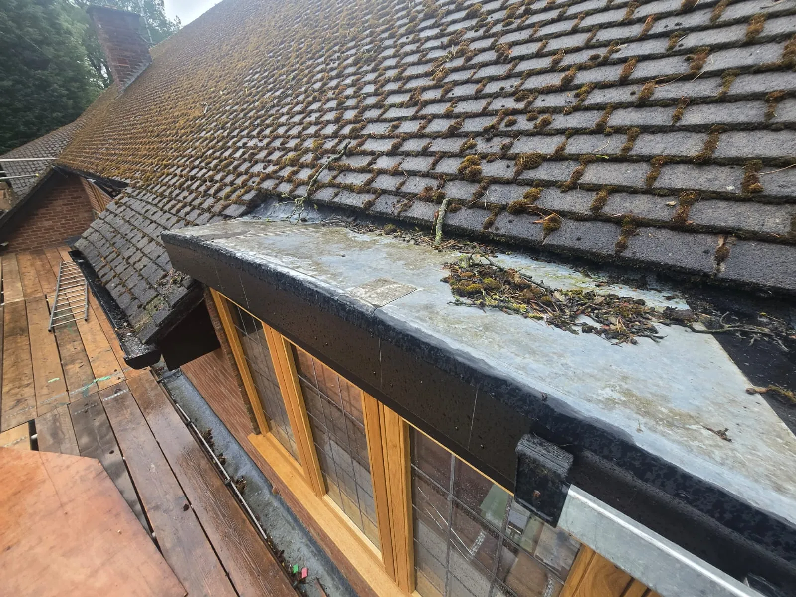 A large, moss-covered tiled roof with a flat roof section below it, also dirty and covered in leaves and twigs, suggesting the need for professional cleaning or repair.