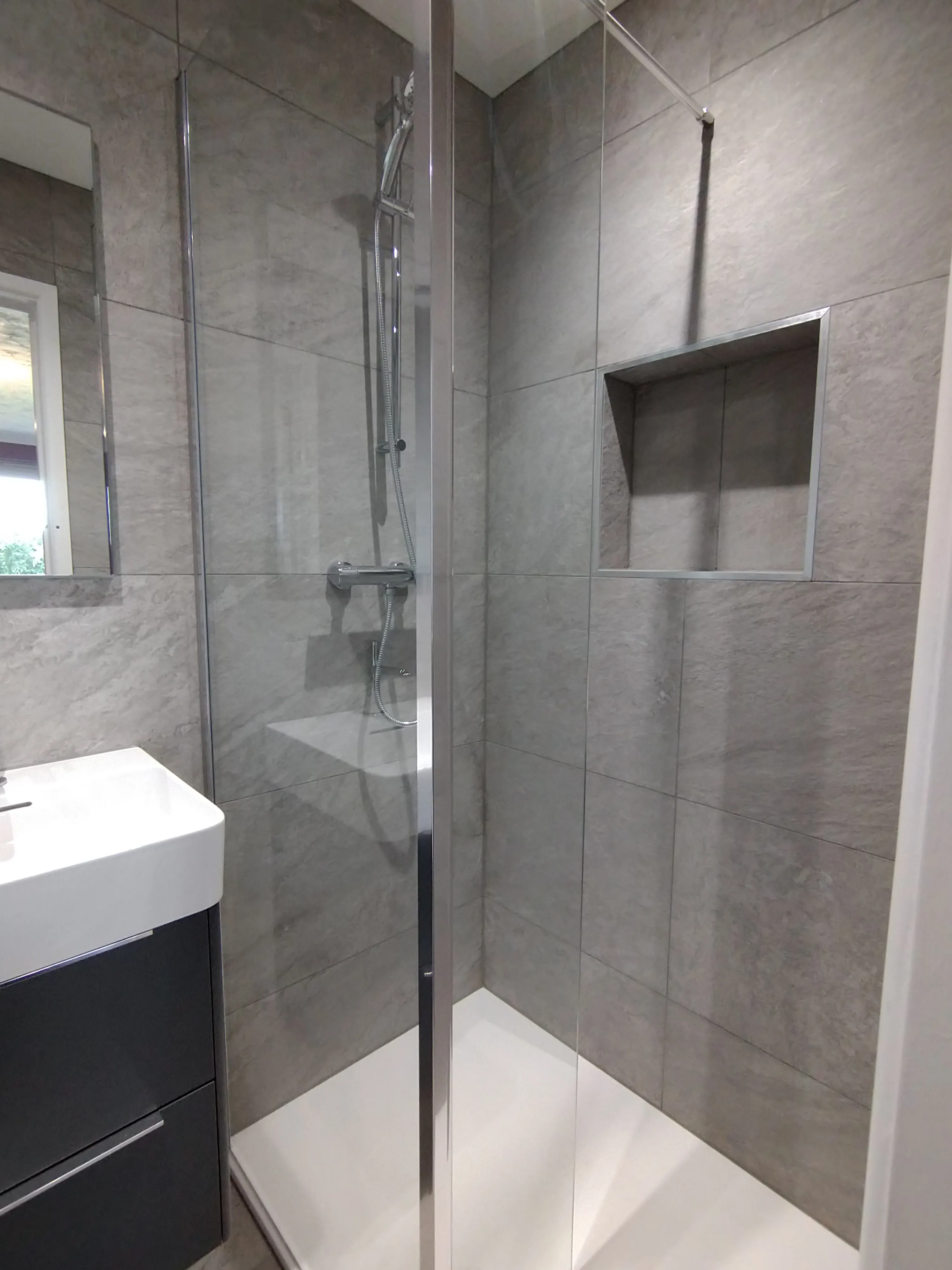 Bespoke luxury walk-in shower installation in Plymouth with grey stone-effect tiles and a recessed shelf by Sands & Vossen.