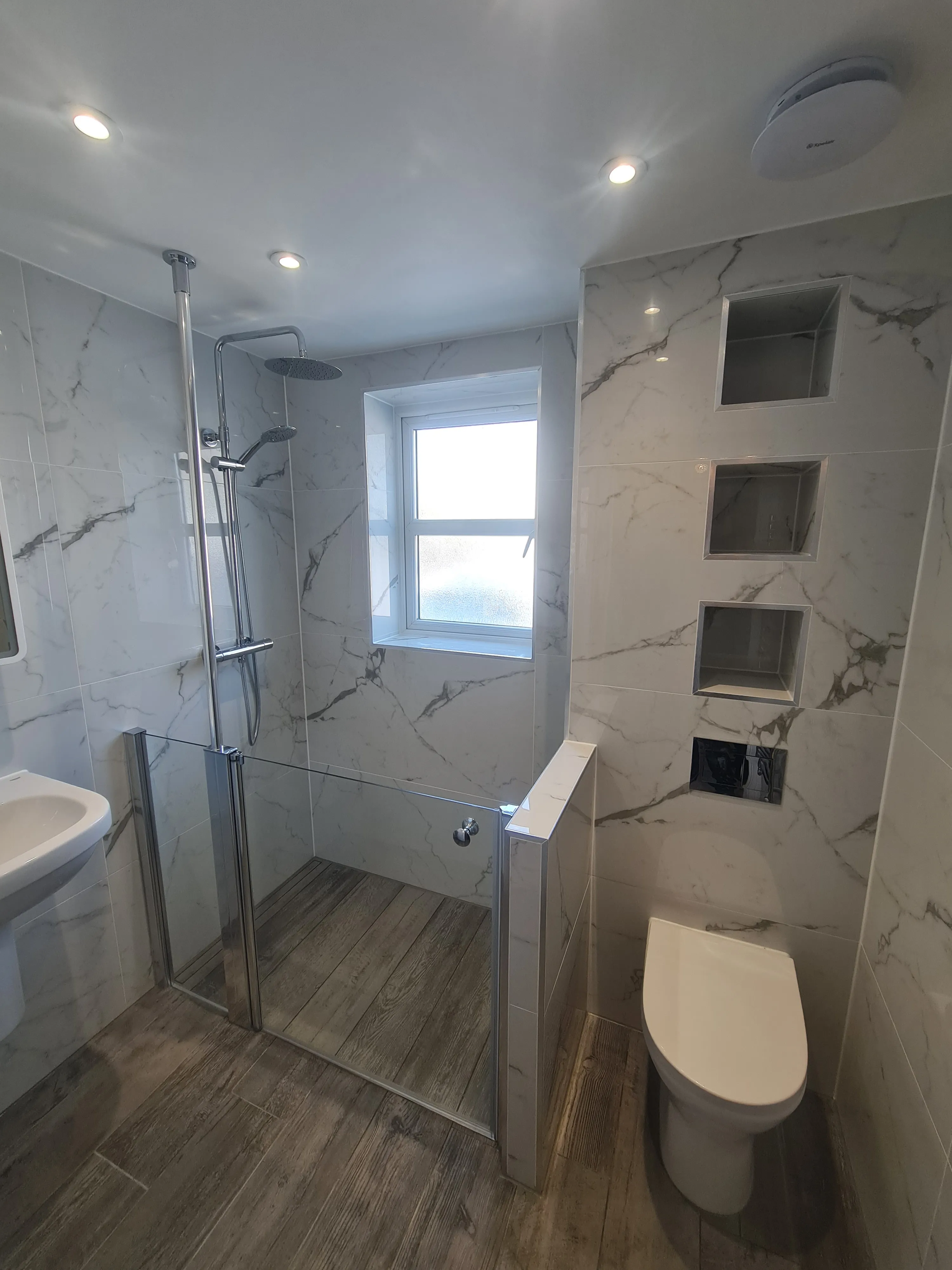 High-end walk-in shower installation in Plymouth with marble-effect tiling and wood-effect flooring by Sands & Vossen.