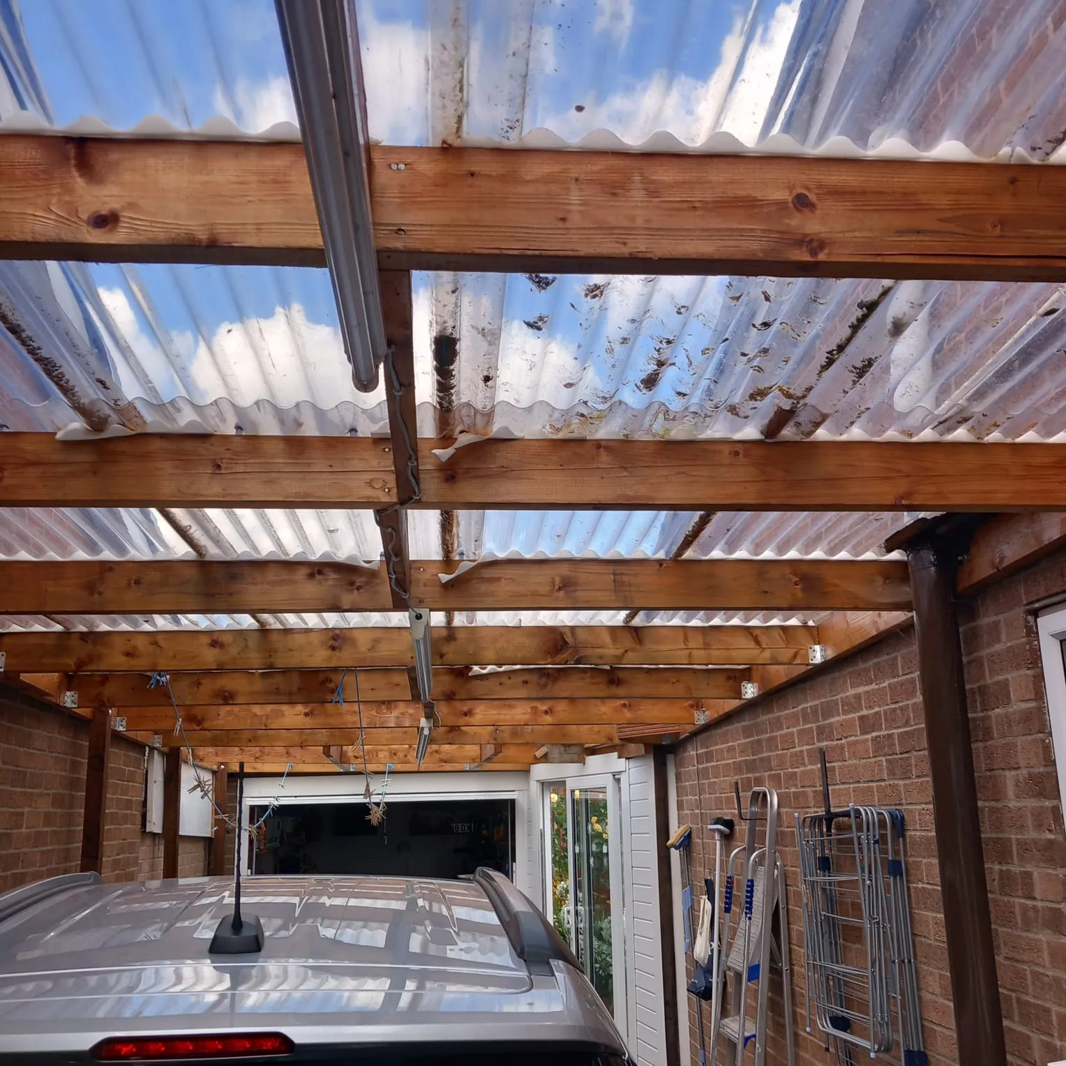 Carport roof with clear corrugated plastic panels, visibly covered in dirt and debris, indicating a need for cleaning or repair.