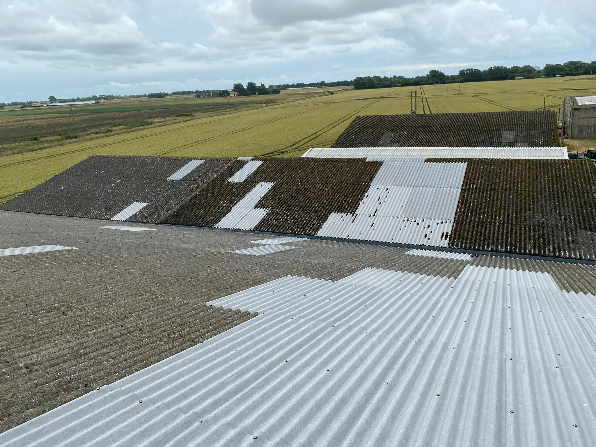 Agricultural barn roof undergoing cladding repairs, contrasting old weathered sections with newly installed weather-resistant corrugated panels