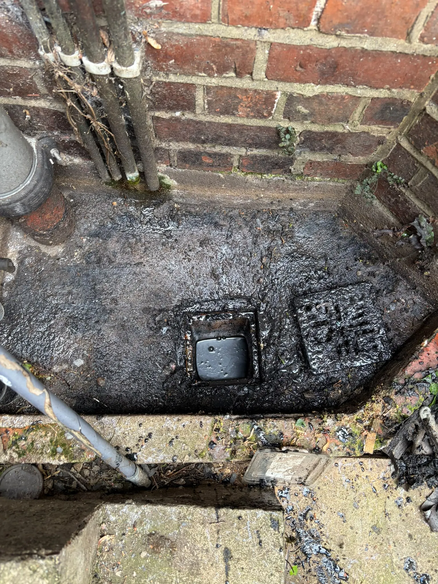 Blocked external drain gully overflowing with silt and wastewater beside a domestic brick property