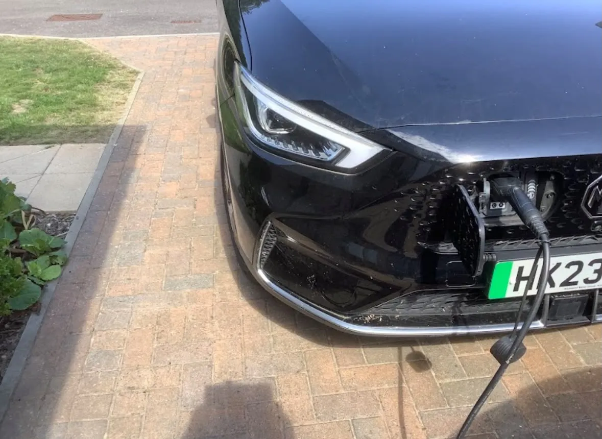 Domestic EV charger cable plugged into an electric vehicle on a residential driveway